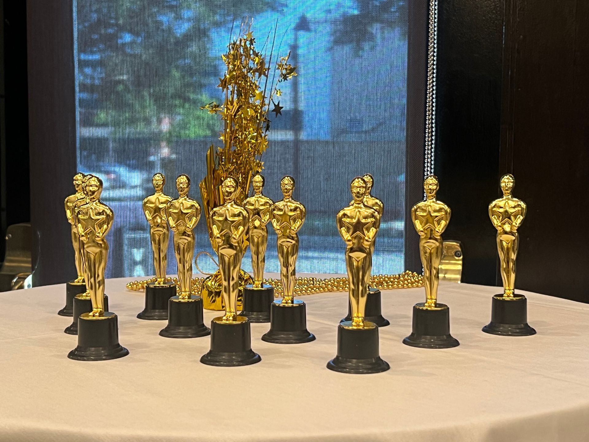 Golden Oscar statuettes on a table, with a decorative gold object behind them, in a dim interior setting.
