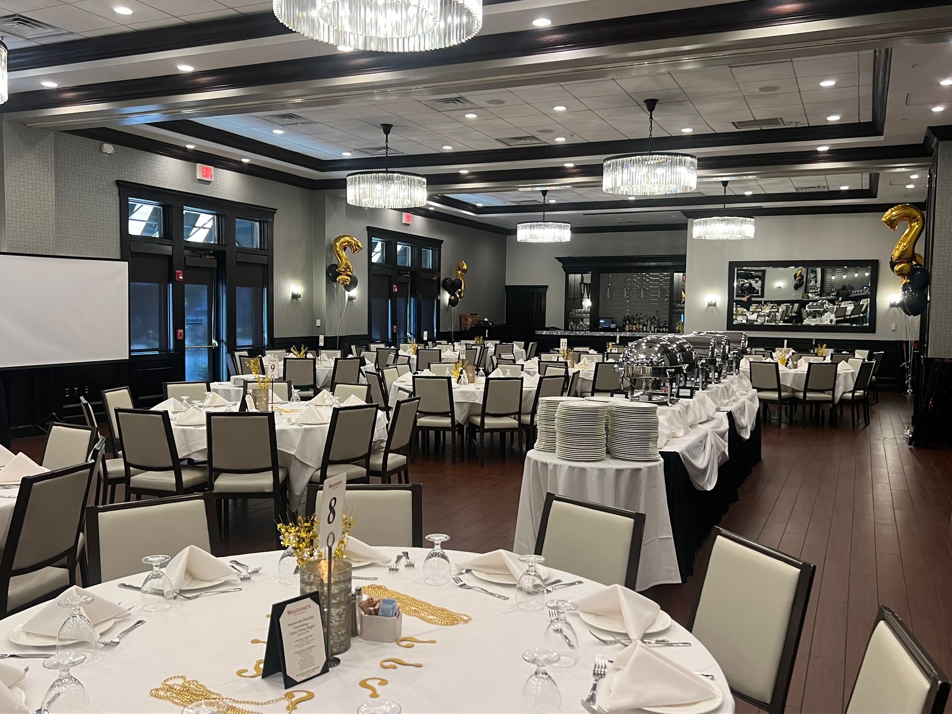 Elegant banquet hall set for a celebration. Round tables with white linens, chairs, and buffet.