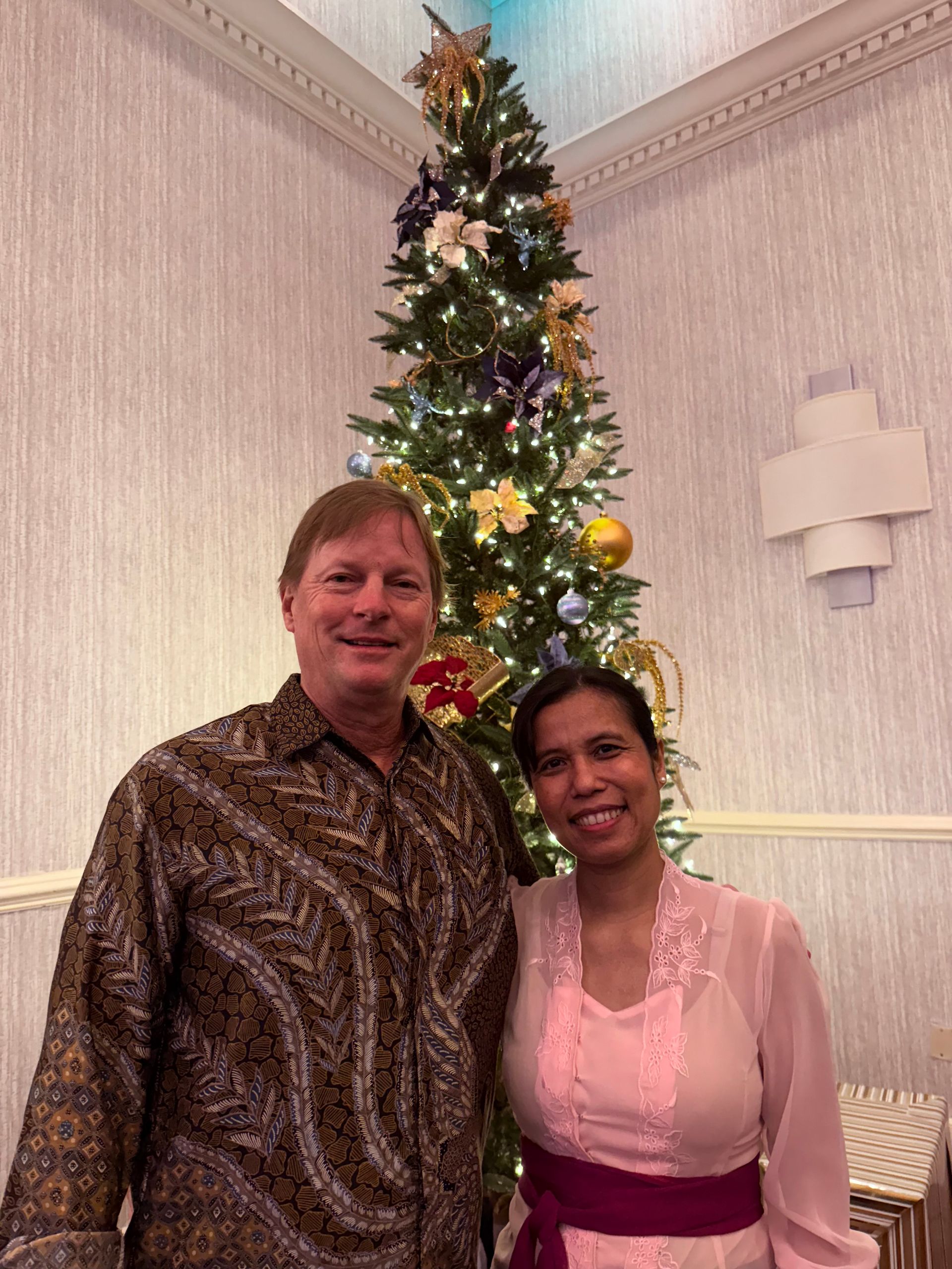 A man and a woman are posing in front of a christmas tree
