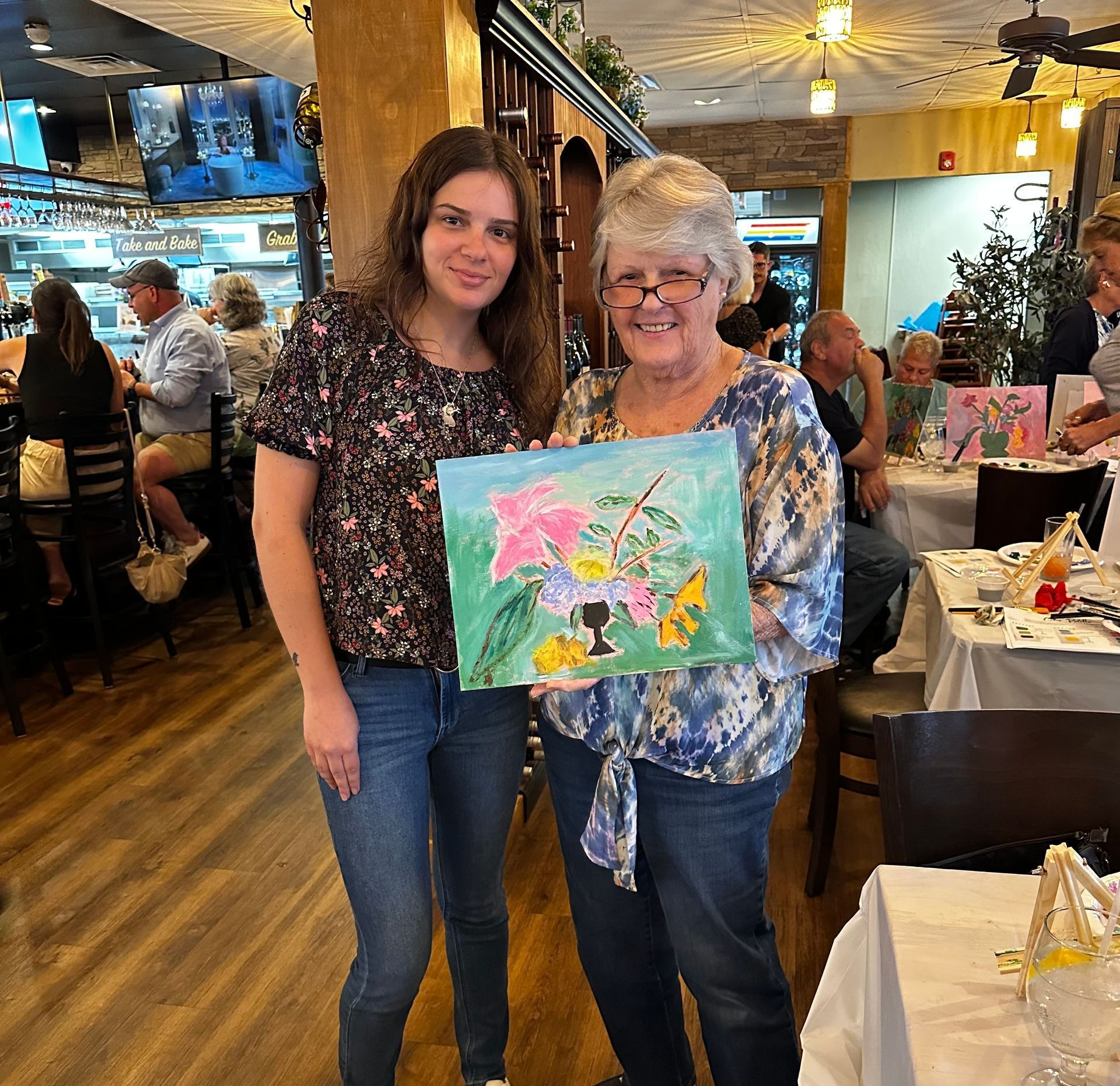 Two women holding a painting in a restaurant