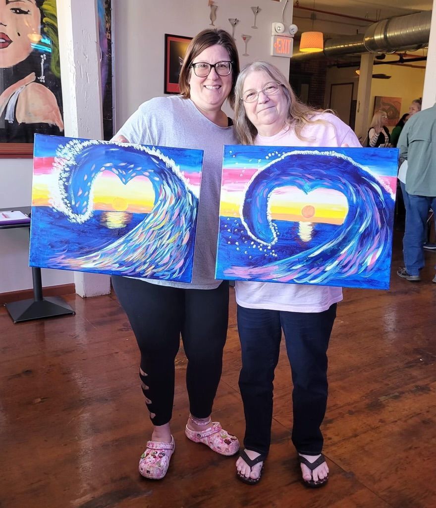 Two women are standing next to each other holding two paintings of waves.