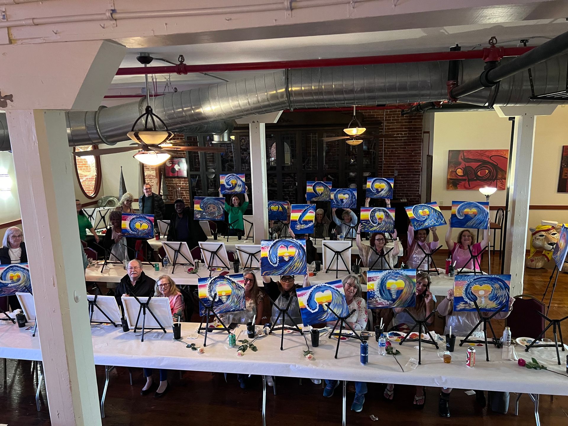 A group of people are sitting at tables with paintings on them