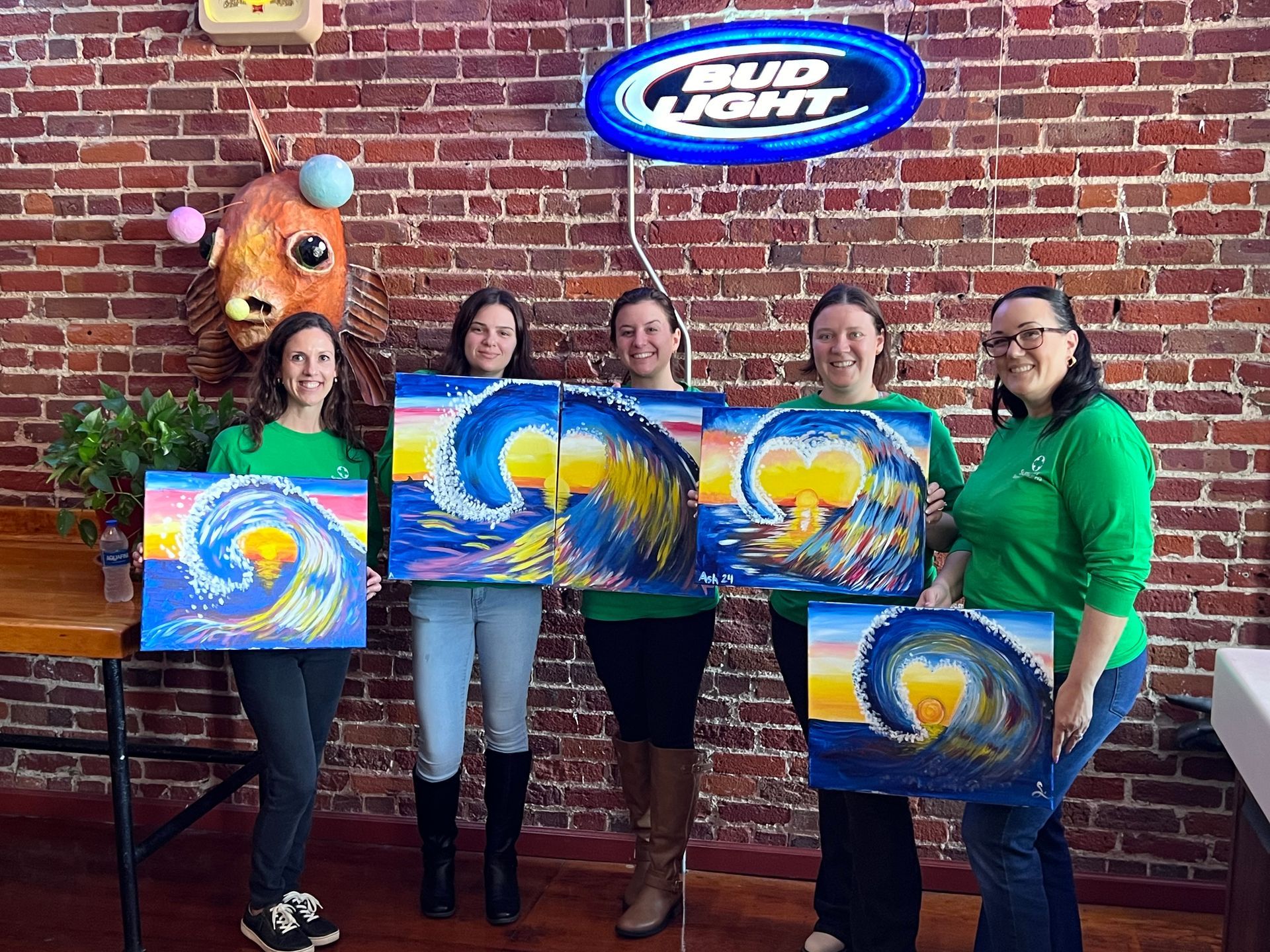 A group of women are holding paintings in front of a bud light sign.