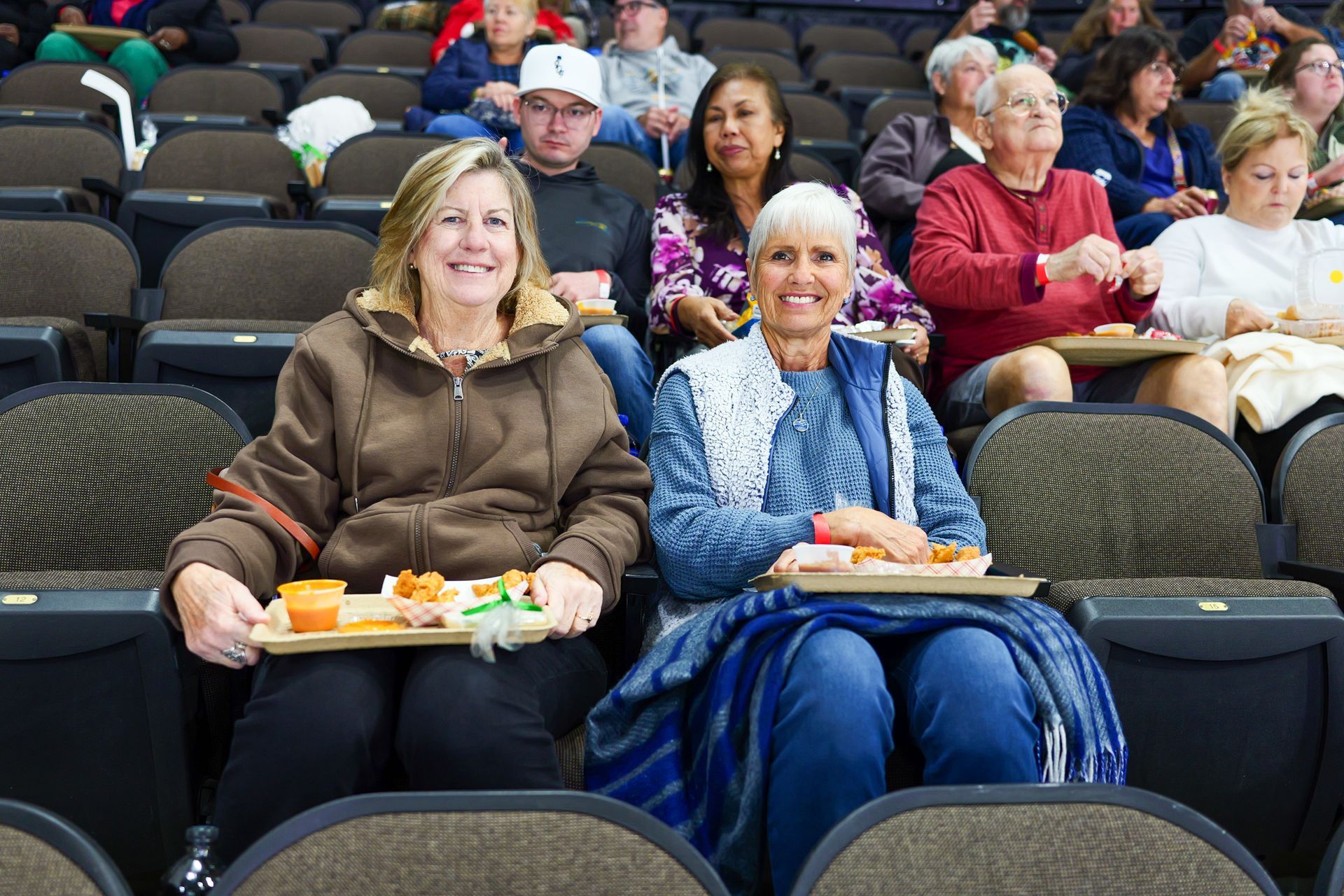 A group of people are sitting in a stadium holding trays of food.