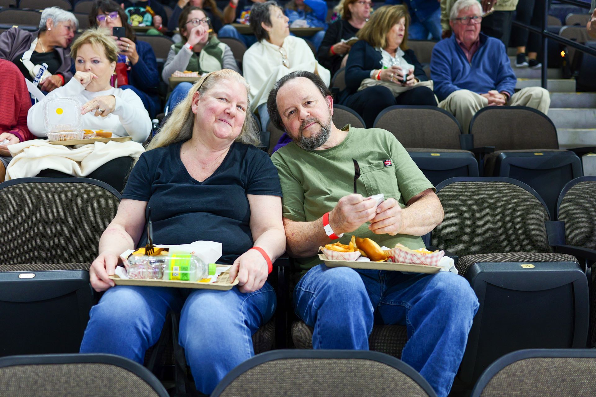 A man and a woman are sitting in a stadium holding trays of food.