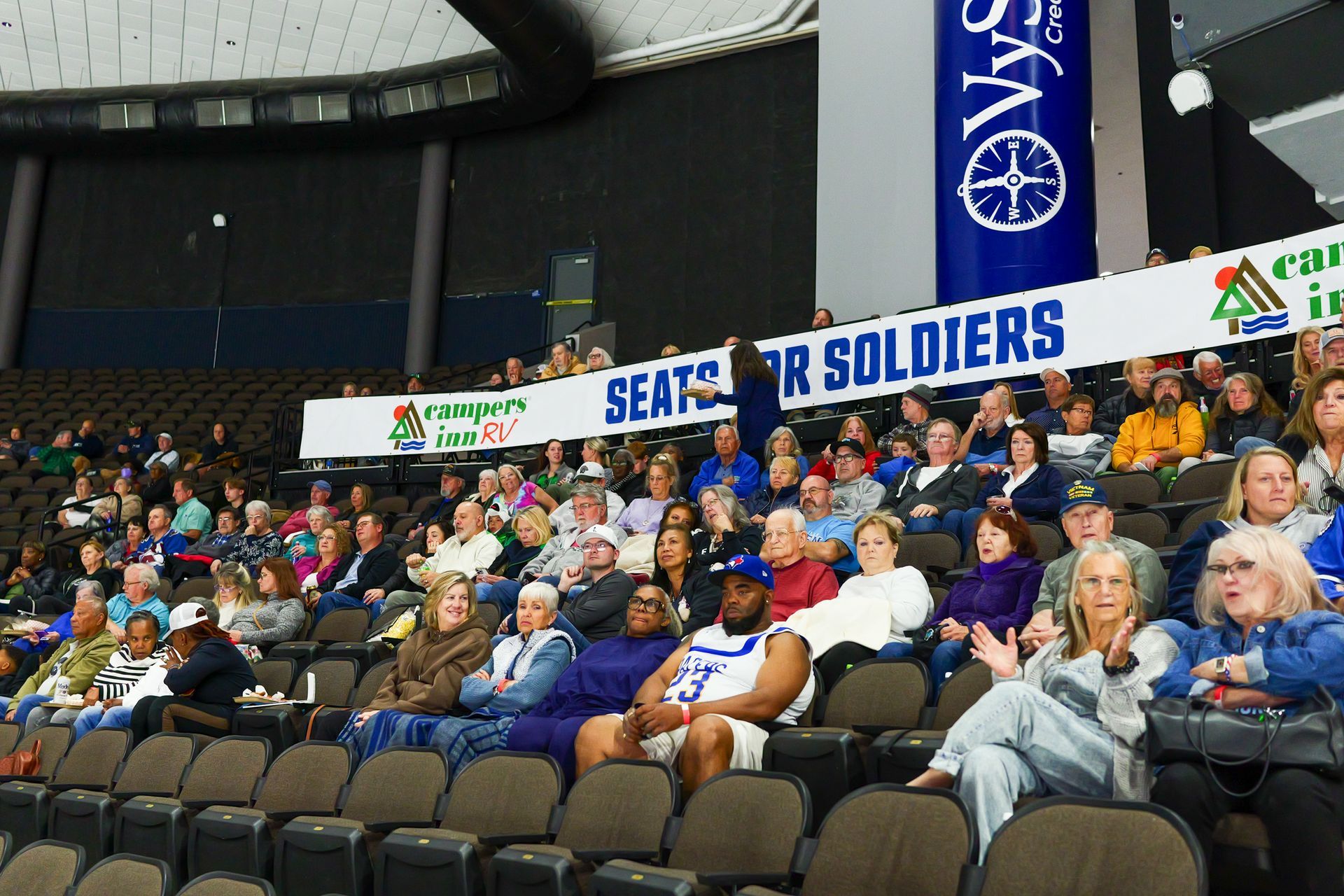 A crowd of people sitting in a stadium with a banner that says seats for soldiers