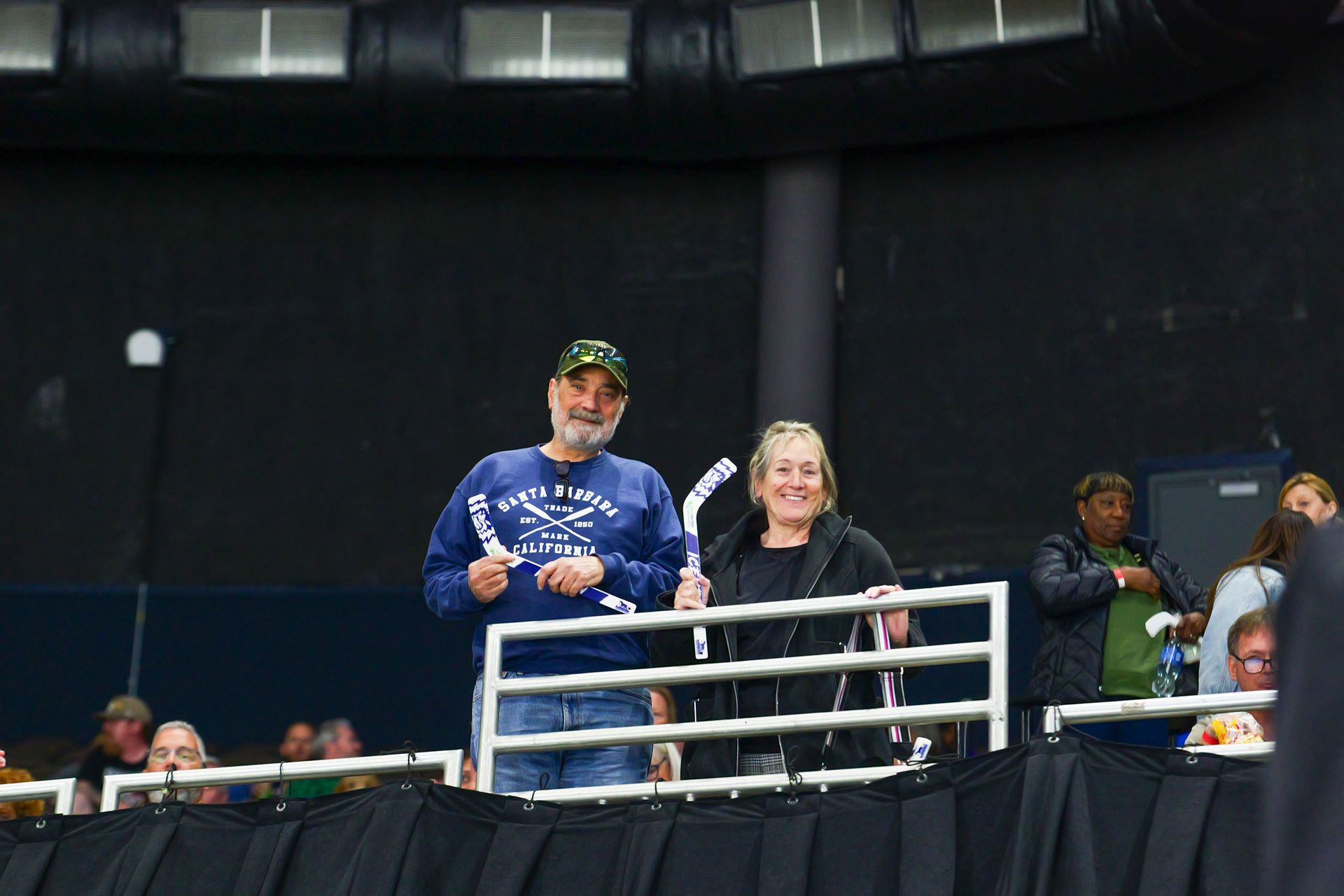 A man and a woman are standing in a stadium holding hockey sticks.