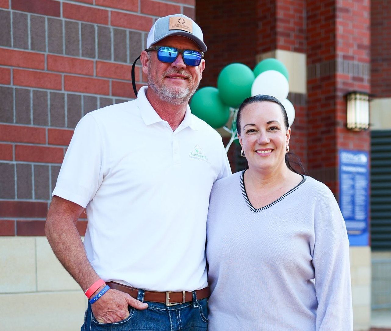 A man and a woman are posing for a picture in front of a brick building.