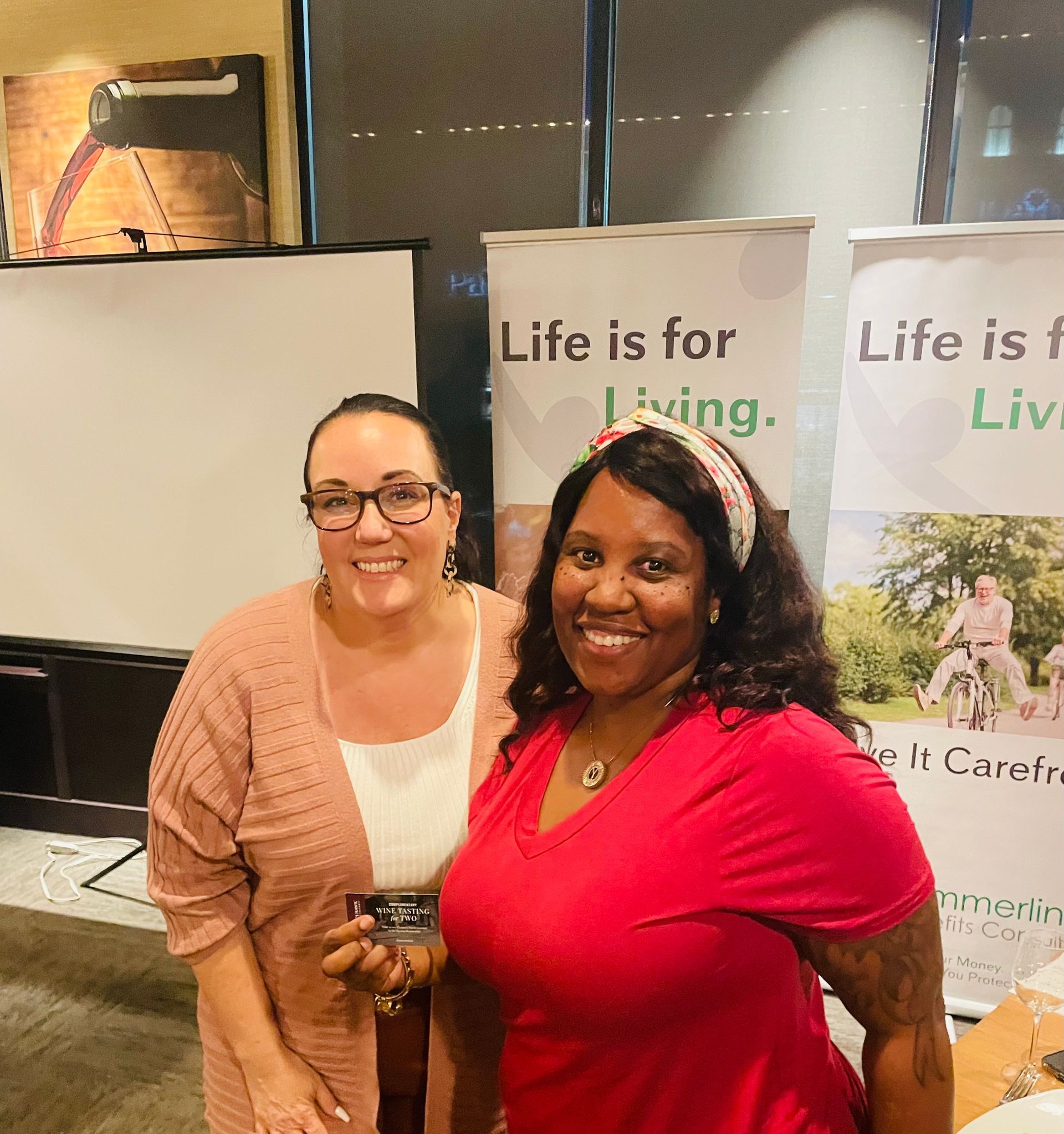 Two women are posing for a picture in front of a sign that says life is for living