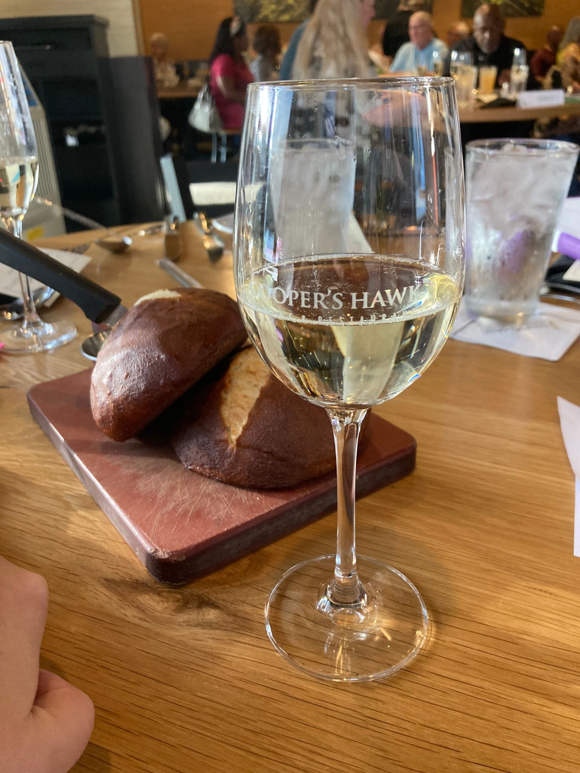 A glass of wine is sitting on a wooden table next to a loaf of bread.