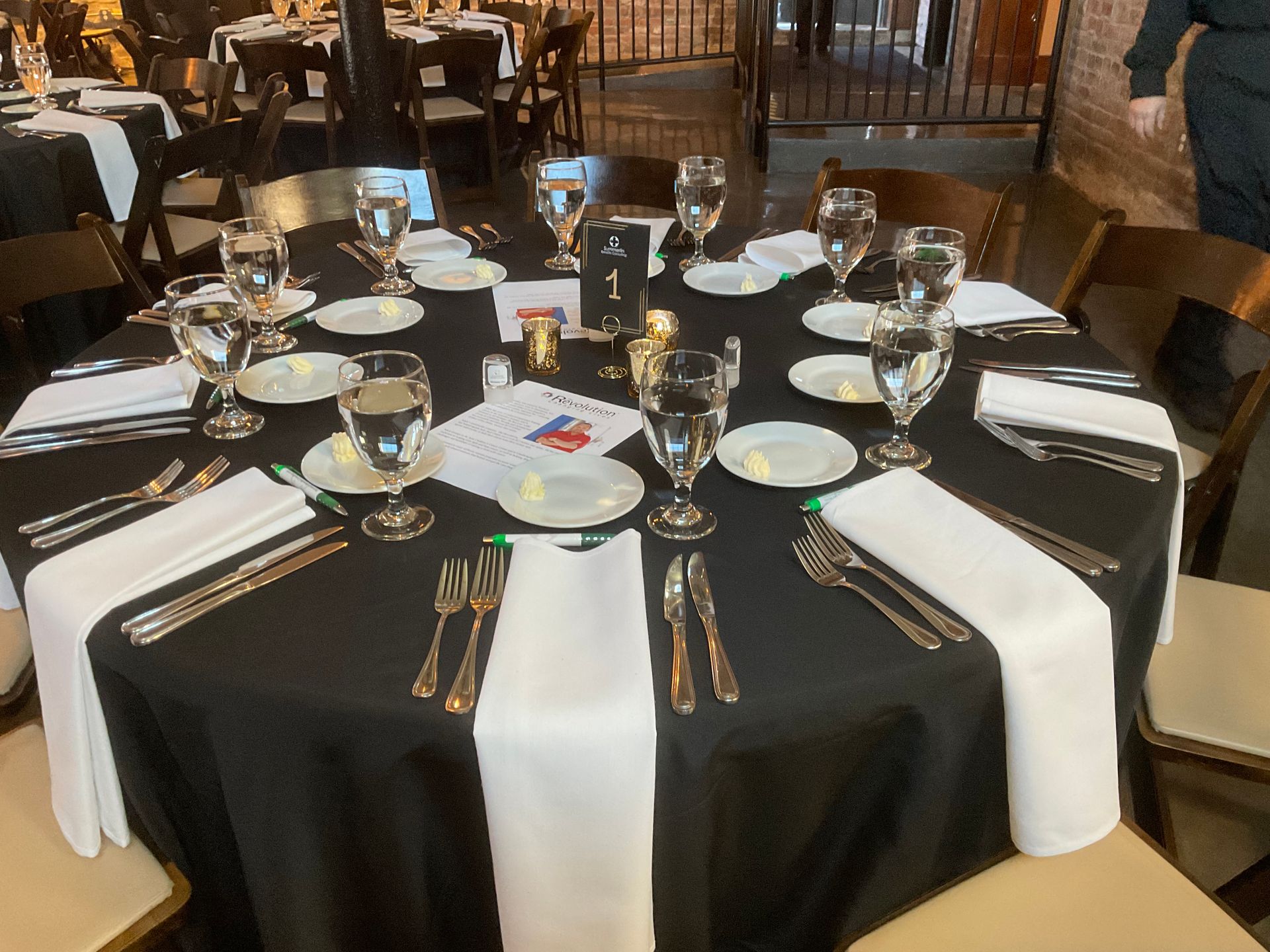 A table with a black table cloth and white napkins is set for a dinner party.