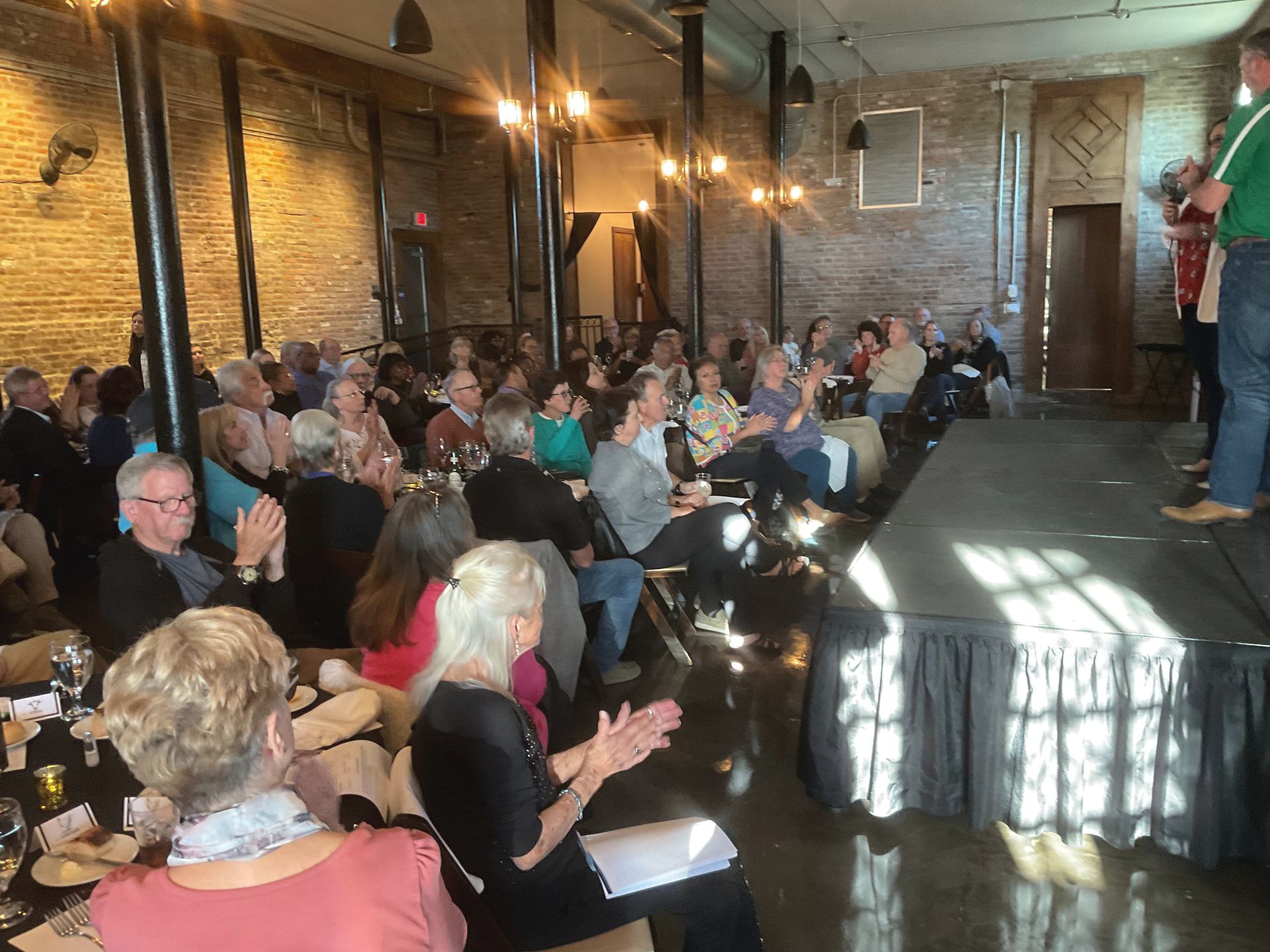A man is standing on a stage in front of a crowd of people applauding.