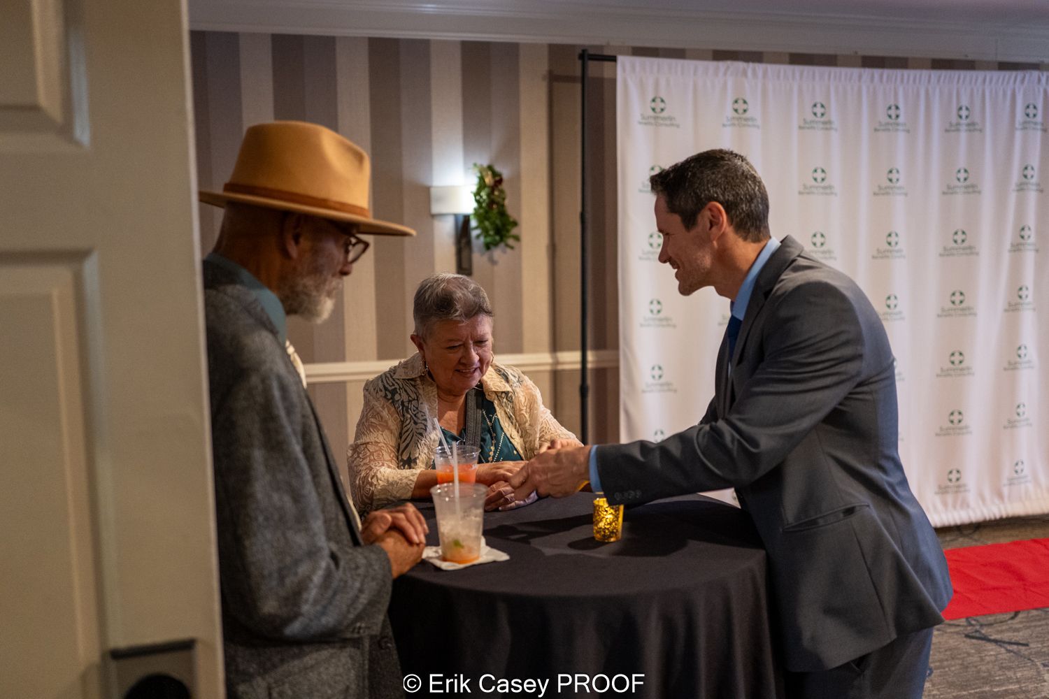 A man in a suit is shaking hands with a woman in a hat.