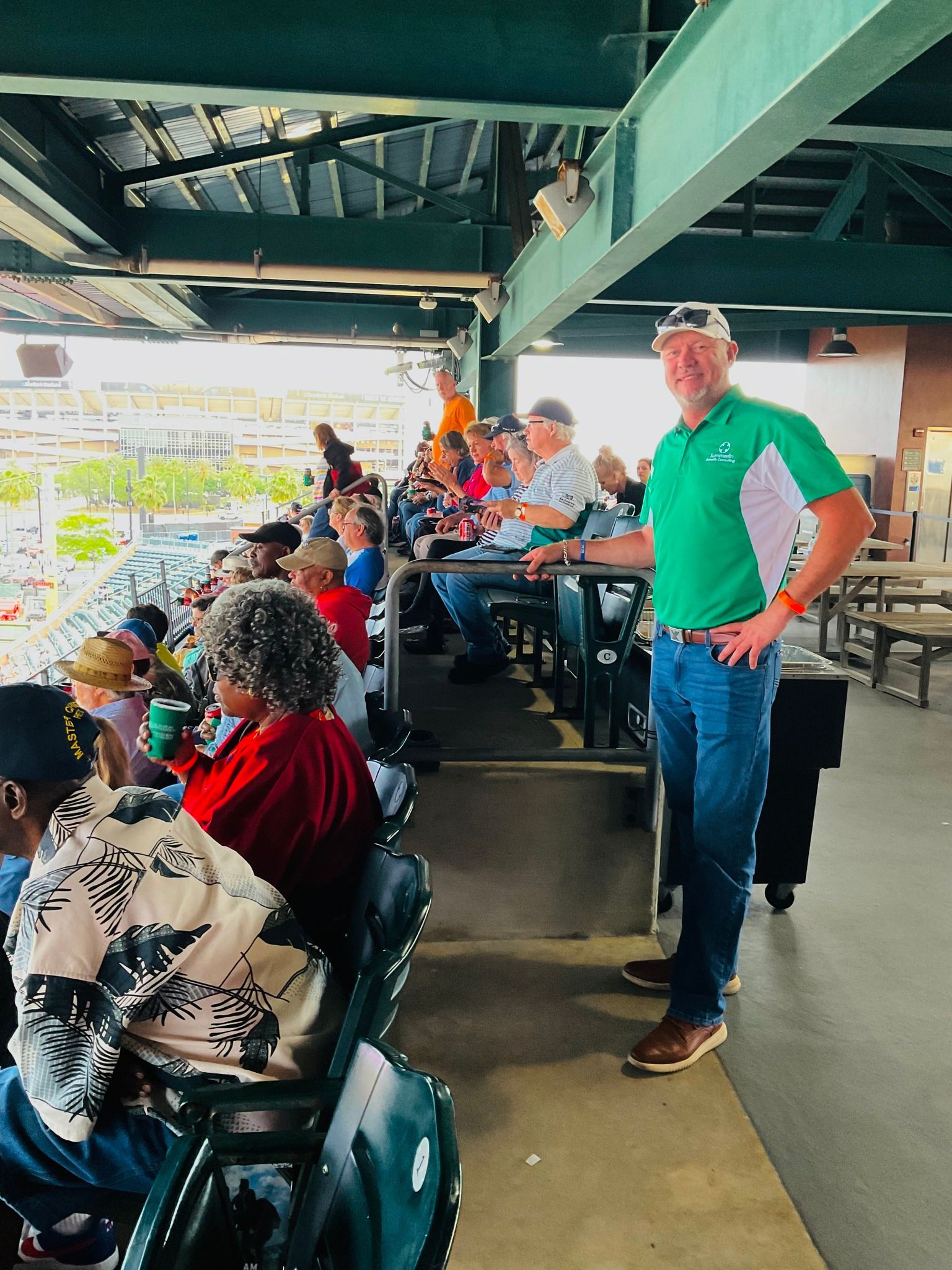 A man in a green shirt is standing in front of a crowd of people sitting in stadium seats.