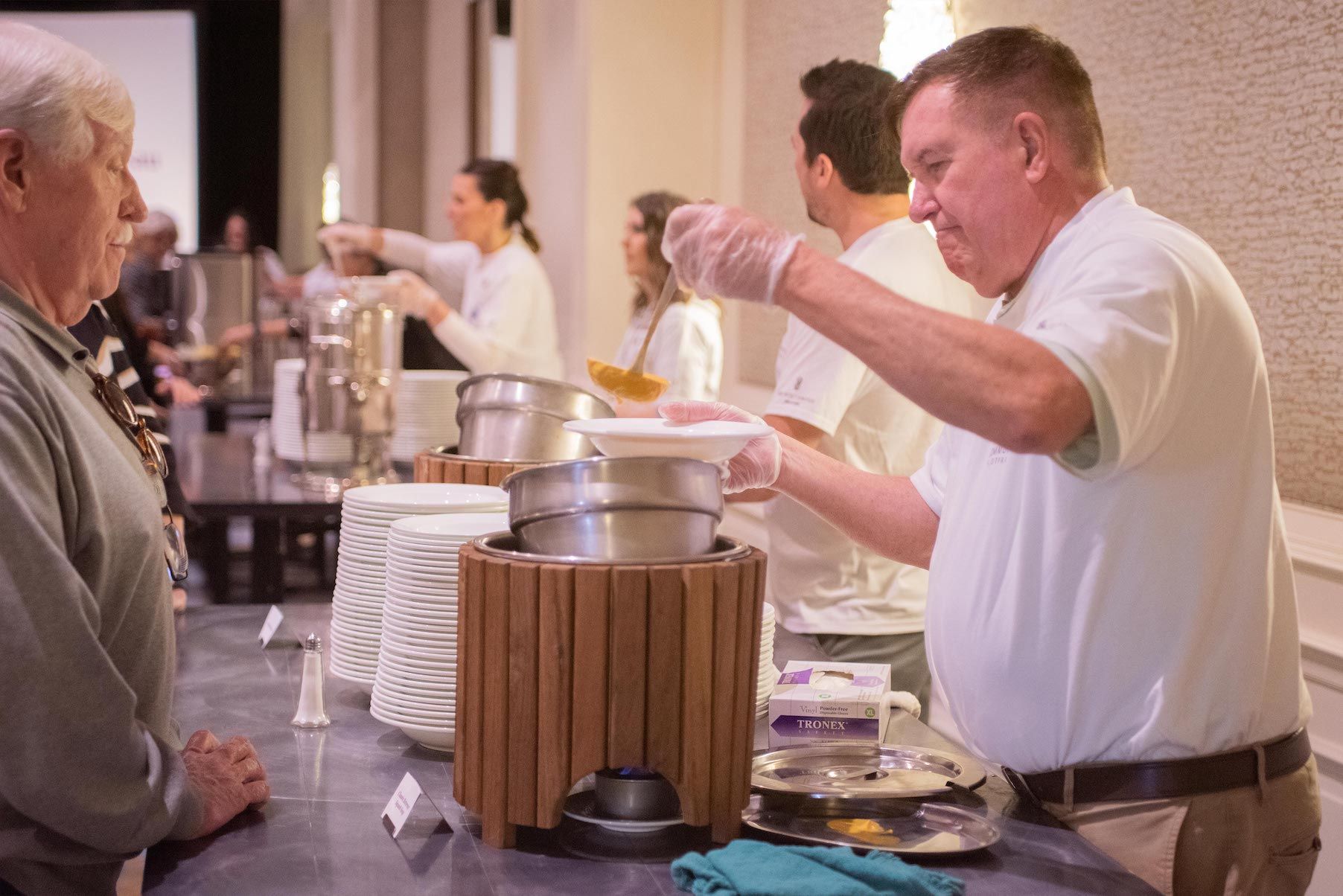 A man is serving food to a group of people at a buffet table.