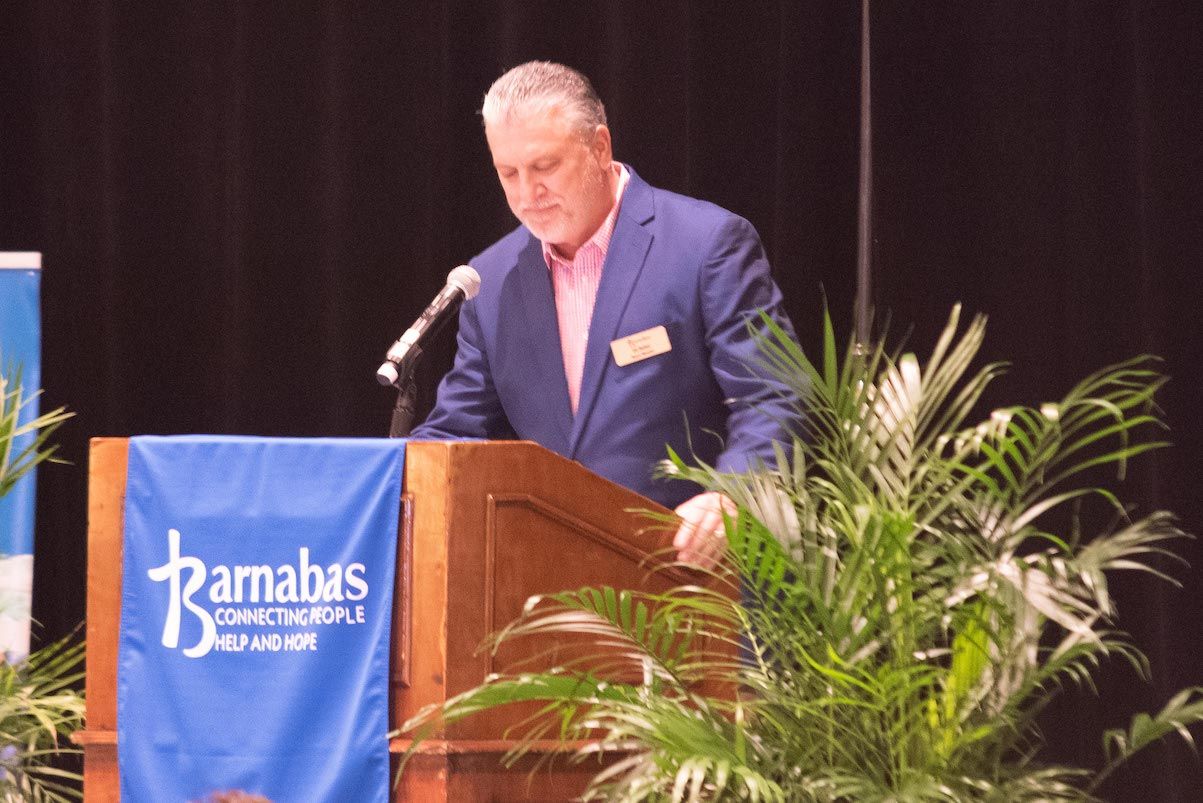 A man stands at a podium with a blue banner that says tamabas