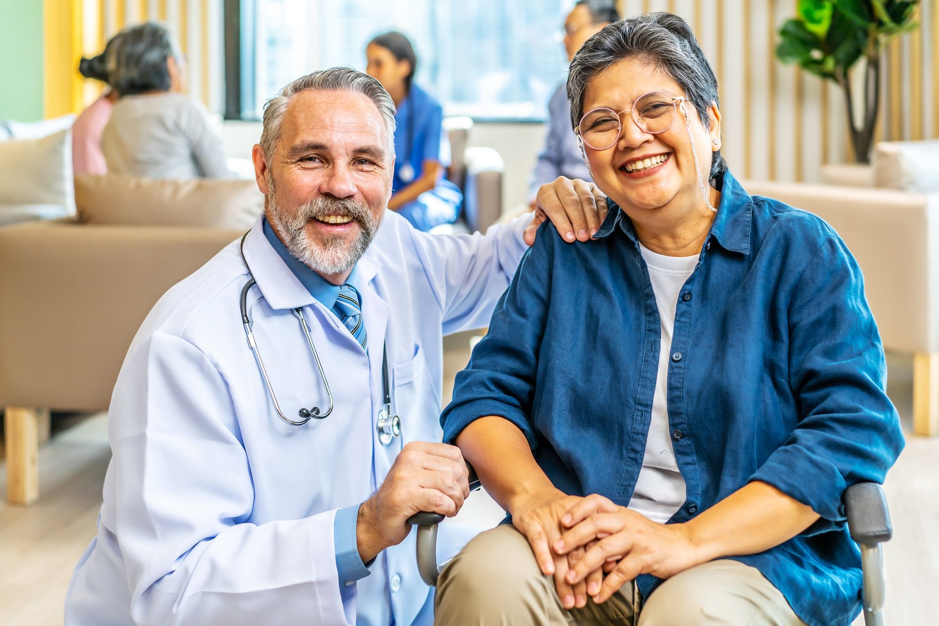 Male doctor crouching down next to older Asian female patient in a wheelchair