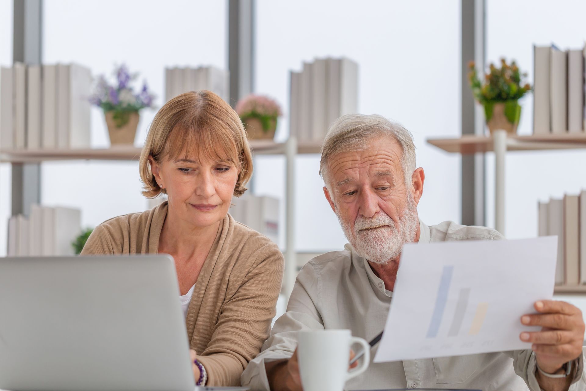 Retired couple sitting in front of a computer looking at a document. Looking slightly concerned.