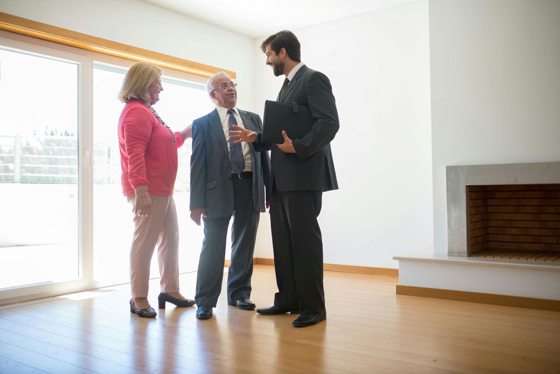 Real estate agent showing a couple a home with fireplace and large windows.