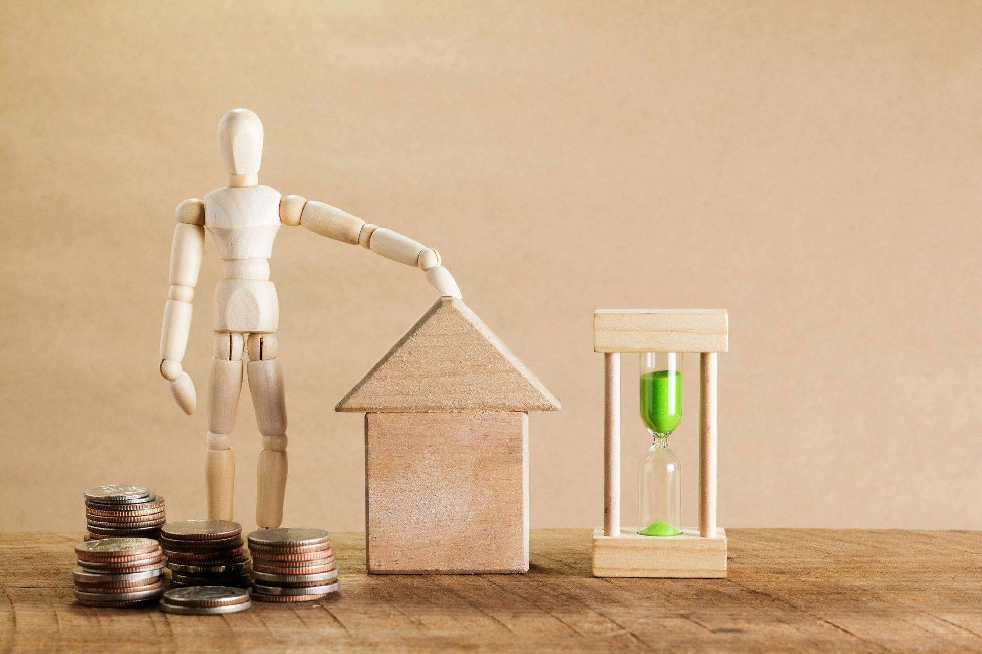Wooden mannequin protecting house model with money and hourglass.
