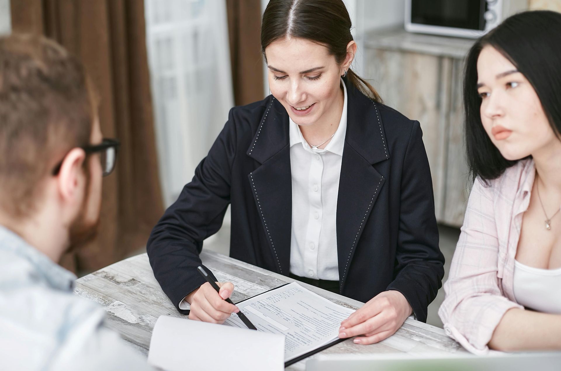 Woman in blazer reviews paperwork with two clients at a table.