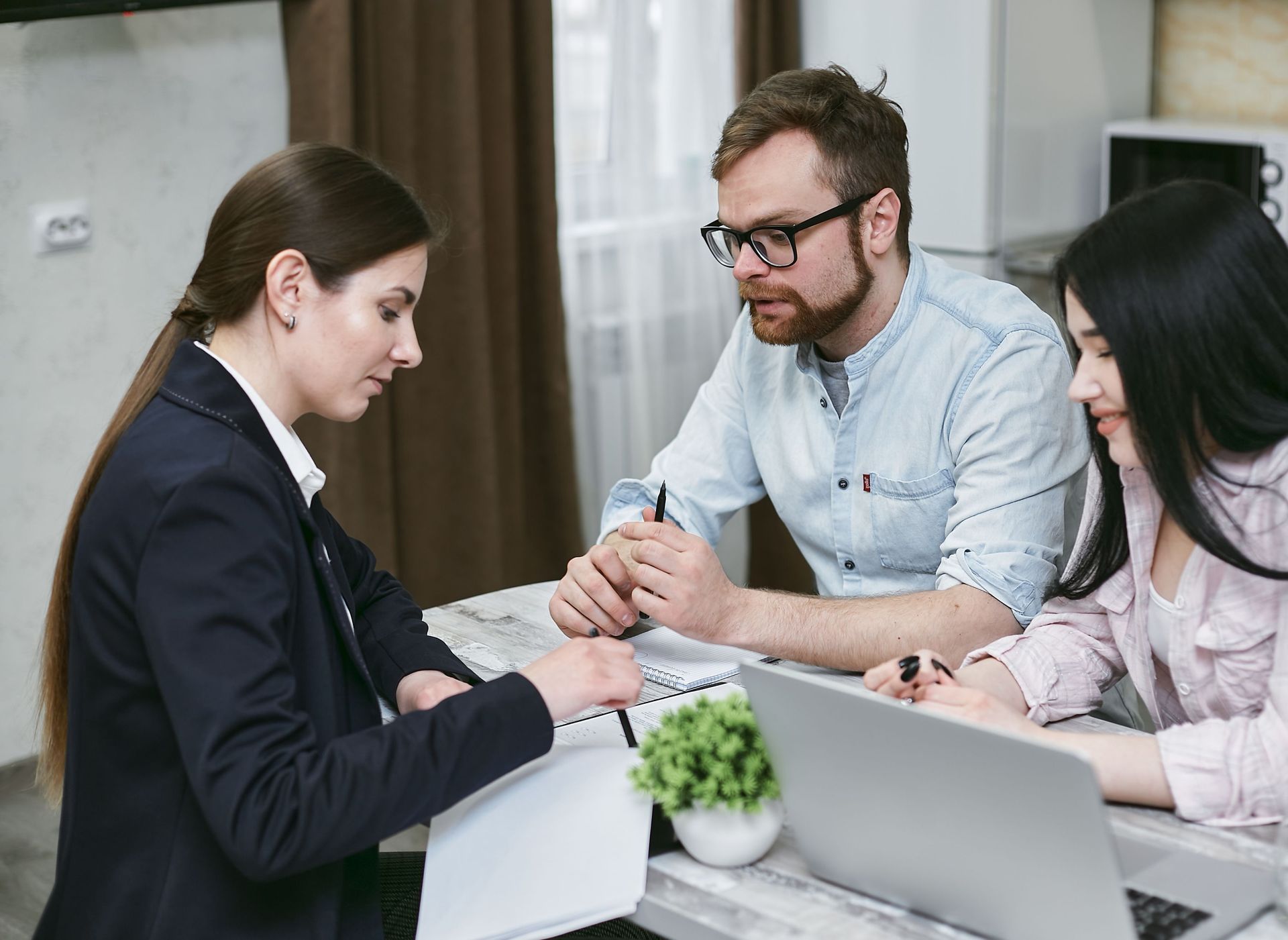 Three coworkers in a meeting, discussing documents around a laptop at a table
