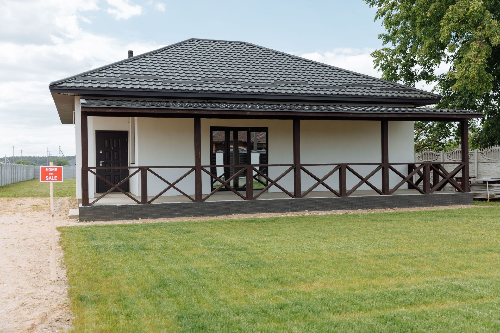 Single-story house with dark roof, white walls, and a wooden porch beside a grassy lawn