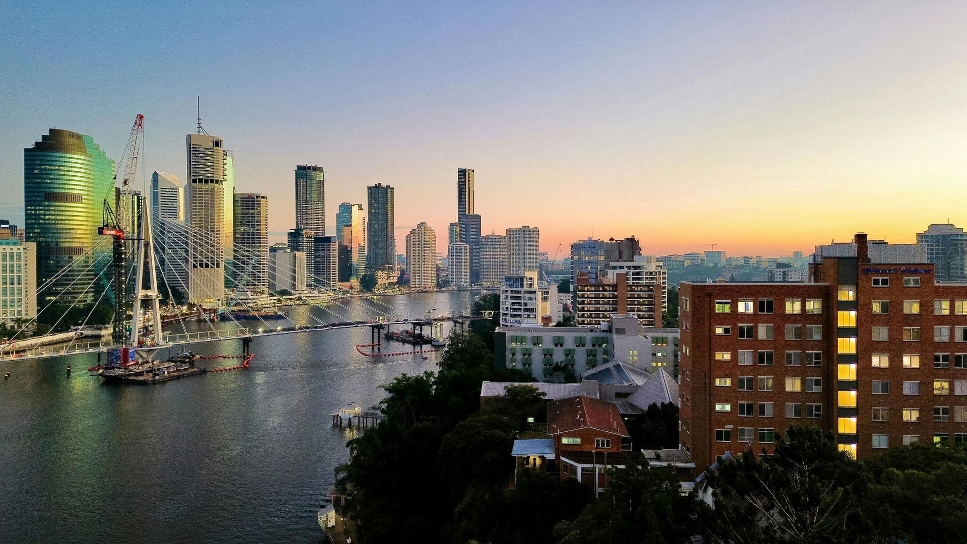 Brisbane skyline at dusk, overlooking the river. Tall buildings silhouetted against an orange and blue sky.
