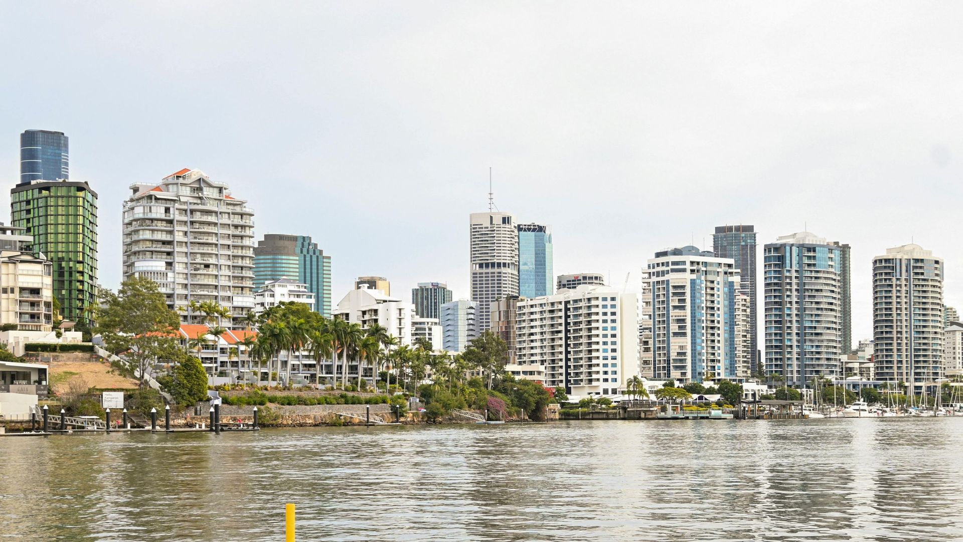 Brisbane, Australia skyline along the river, featuring high-rise buildings and trees on the water's edge.