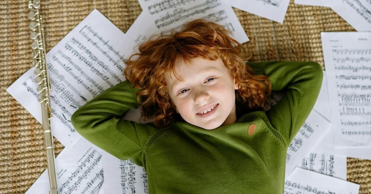 Write a Musical - a young child is lying on the floor surrounded by sheet music and a flute.