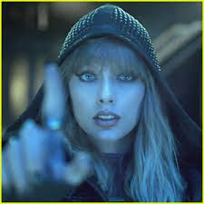 taylor swift is wearing a black hat and hood and pointing at the camera.