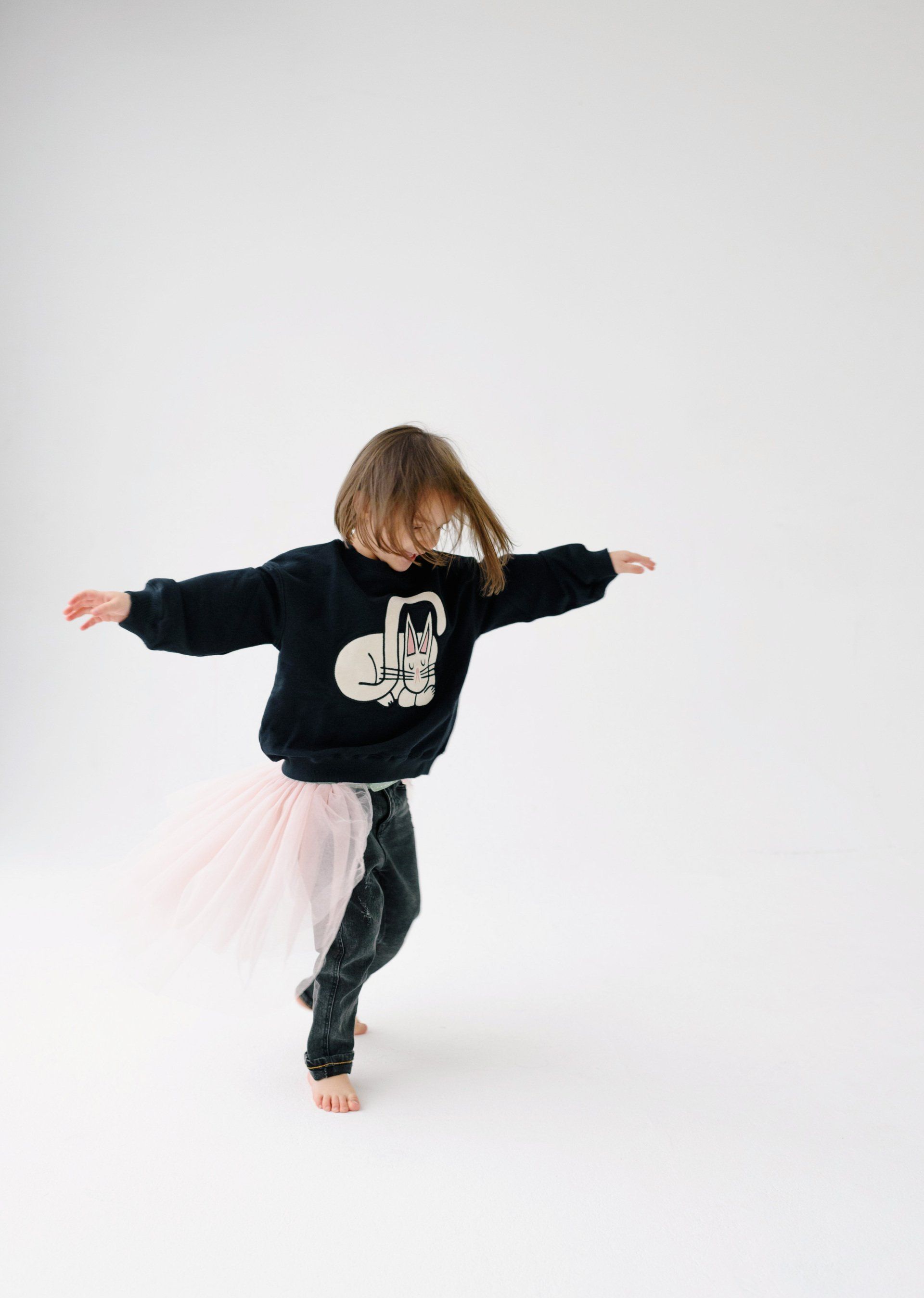 a little girl in a black sweater and a pink tutu is dancing .