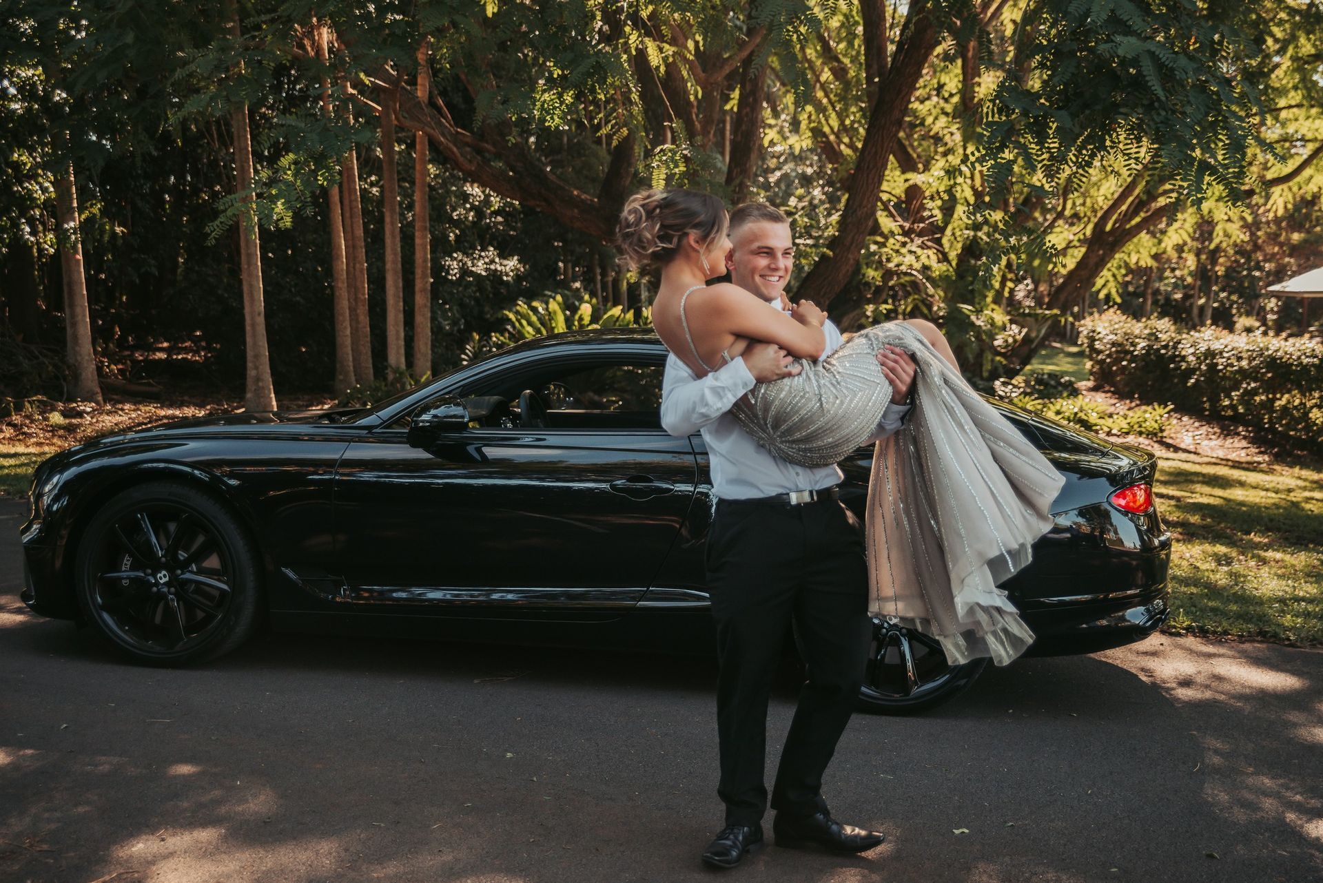 Man Carrying Woman in Formal Attire Near a Black Car — Feathers & Lace Photography in Tarzali, QLD