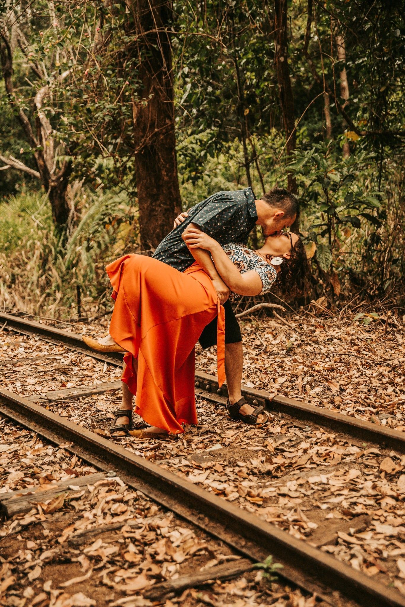 Woman in Orange Skirt Leans Back as Man Holds Her While Kissing — Feathers & Lace Photography in Tarzali, QLD