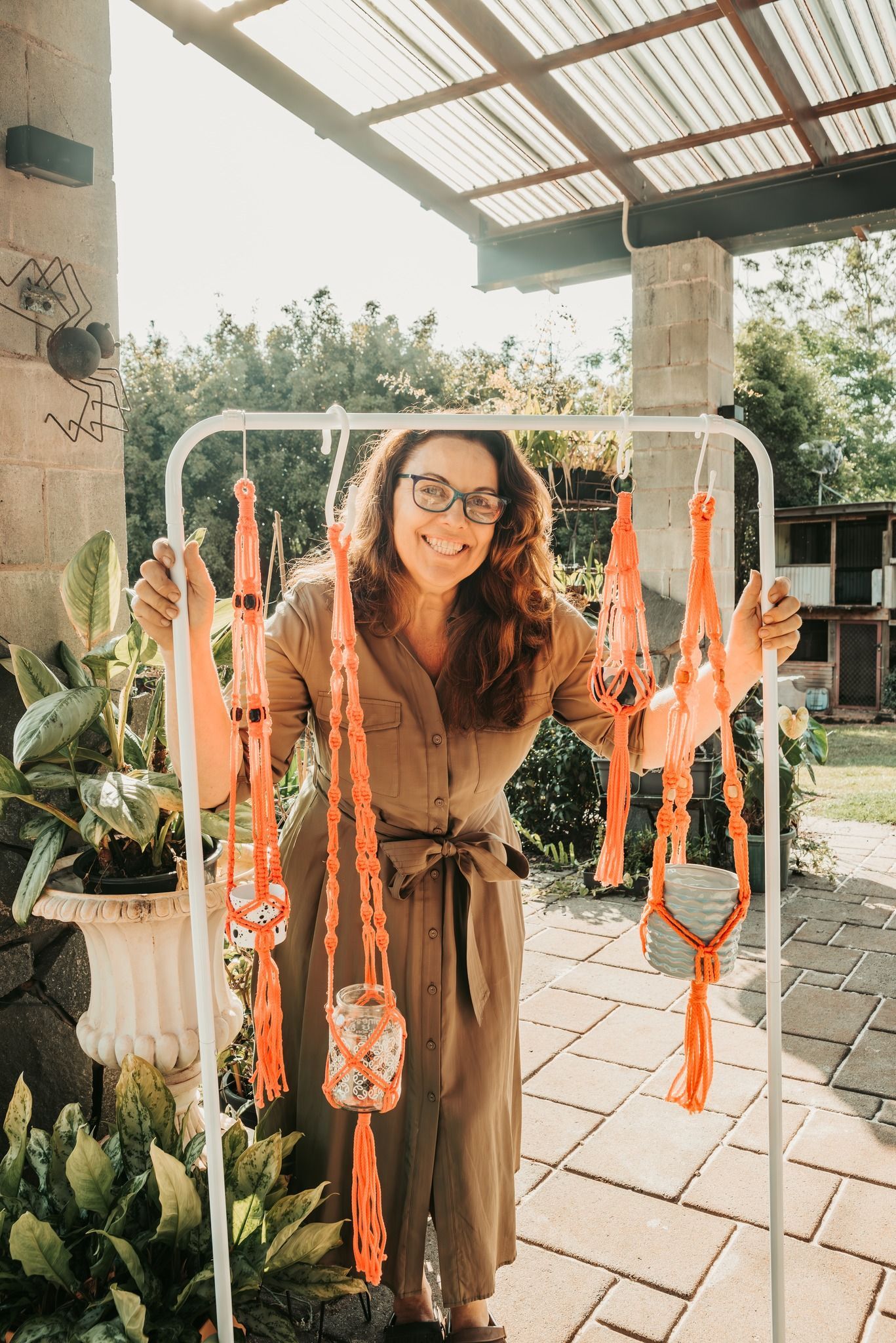 Woman in Glasses Smiles, Displaying Orange Macrame Plant — Feathers & Lace Photography in Tarzali, QLD