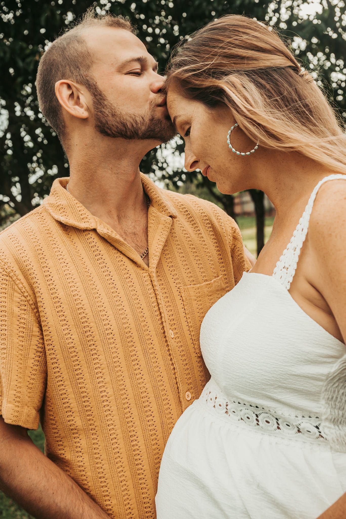 Man Kissing Pregnant Woman's Forehead; Both in Casual Clothes Outdoors — Feathers & Lace Photography in Tarzali, QLD