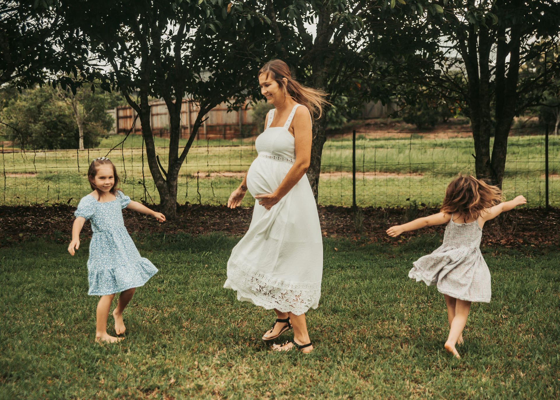 Pregnant Person Dances With Two Children in a Grassy Yard — Feathers & Lace Photography in Tarzali, QLD