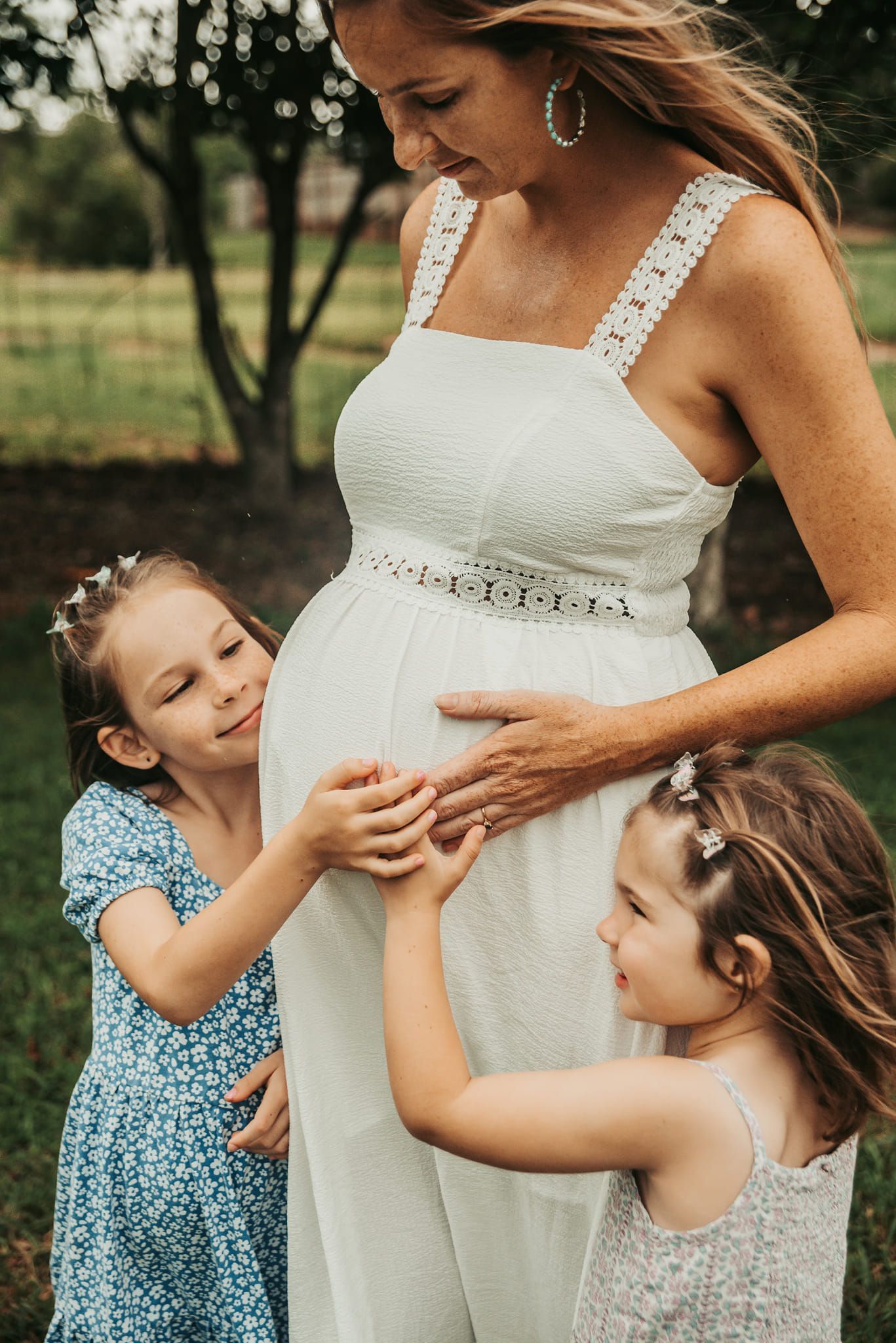 Pregnant Woman in White Dress, Embraced by Two Young Girls — Feathers & Lace Photography in Tarzali, QLD