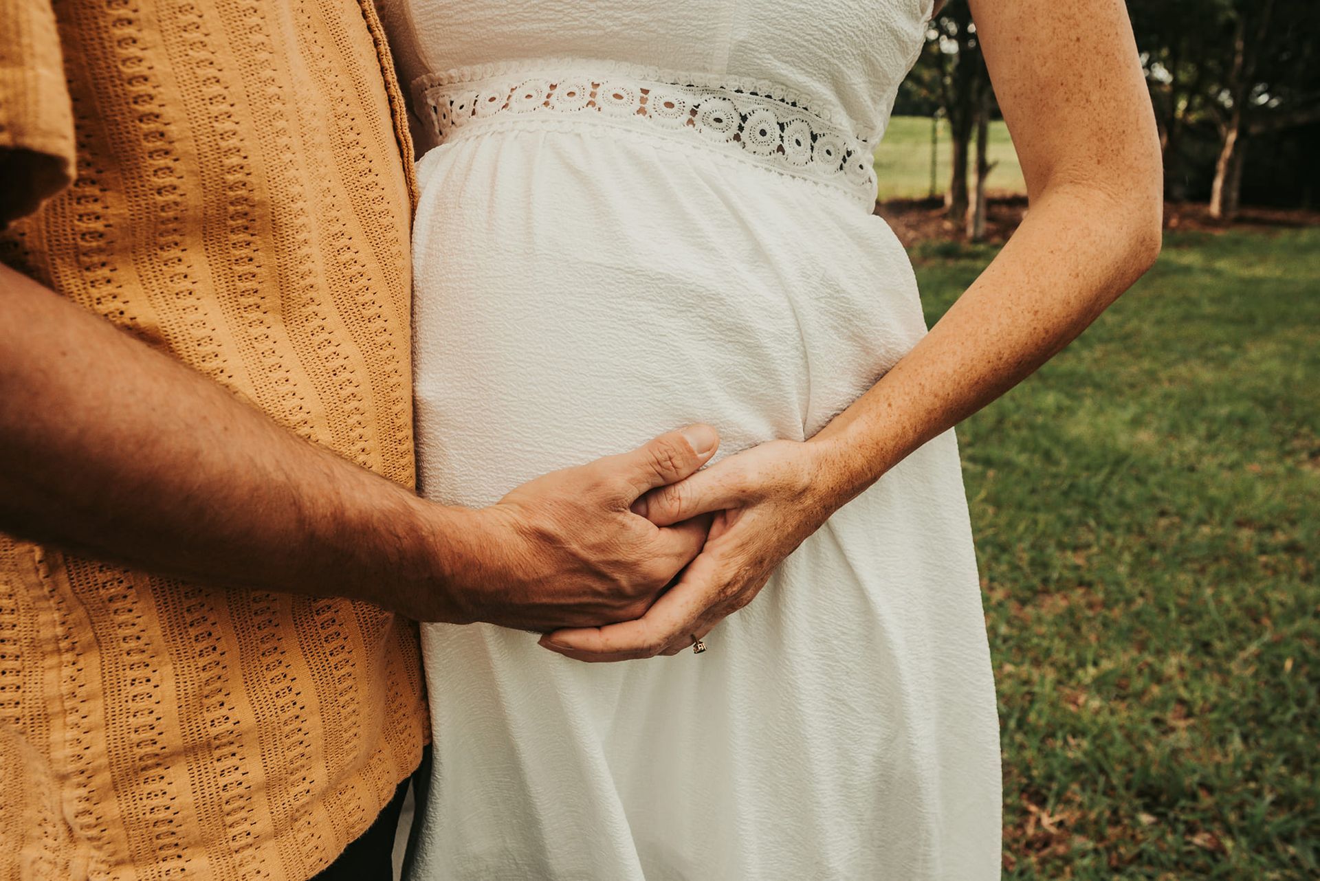 Pregnant Woman in White Dress, Hands Clasped Over Belly — Feathers & Lace Photography in Tarzali, QLD