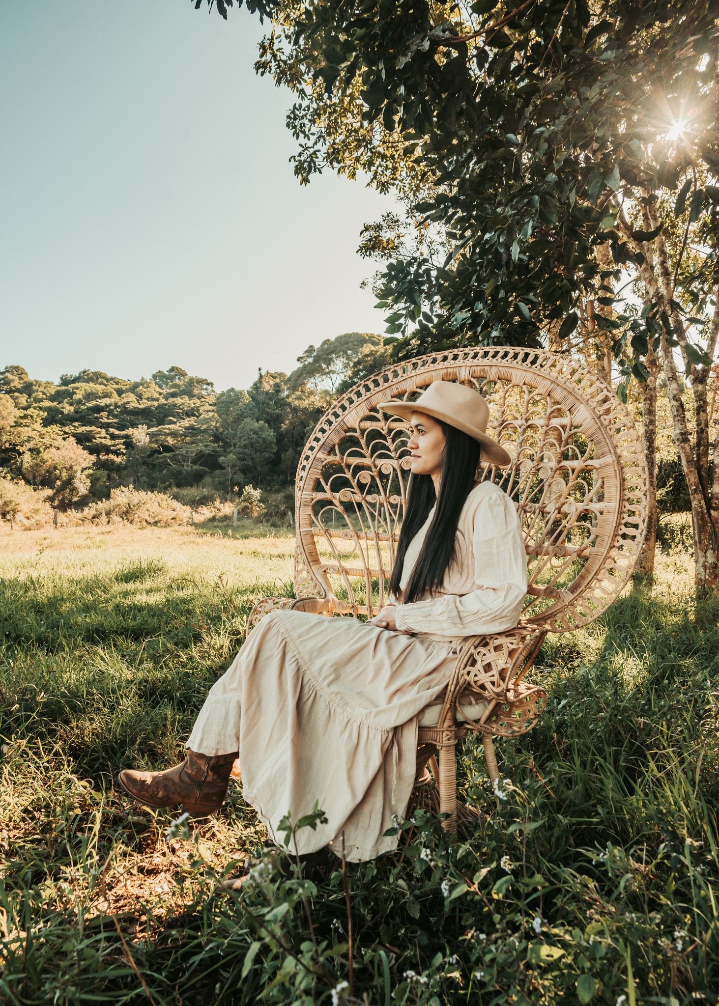 Woman in a White Dress and Hat Sits in a Round Woven Chair — Feathers & Lace Photography in Tarzali, QLD
