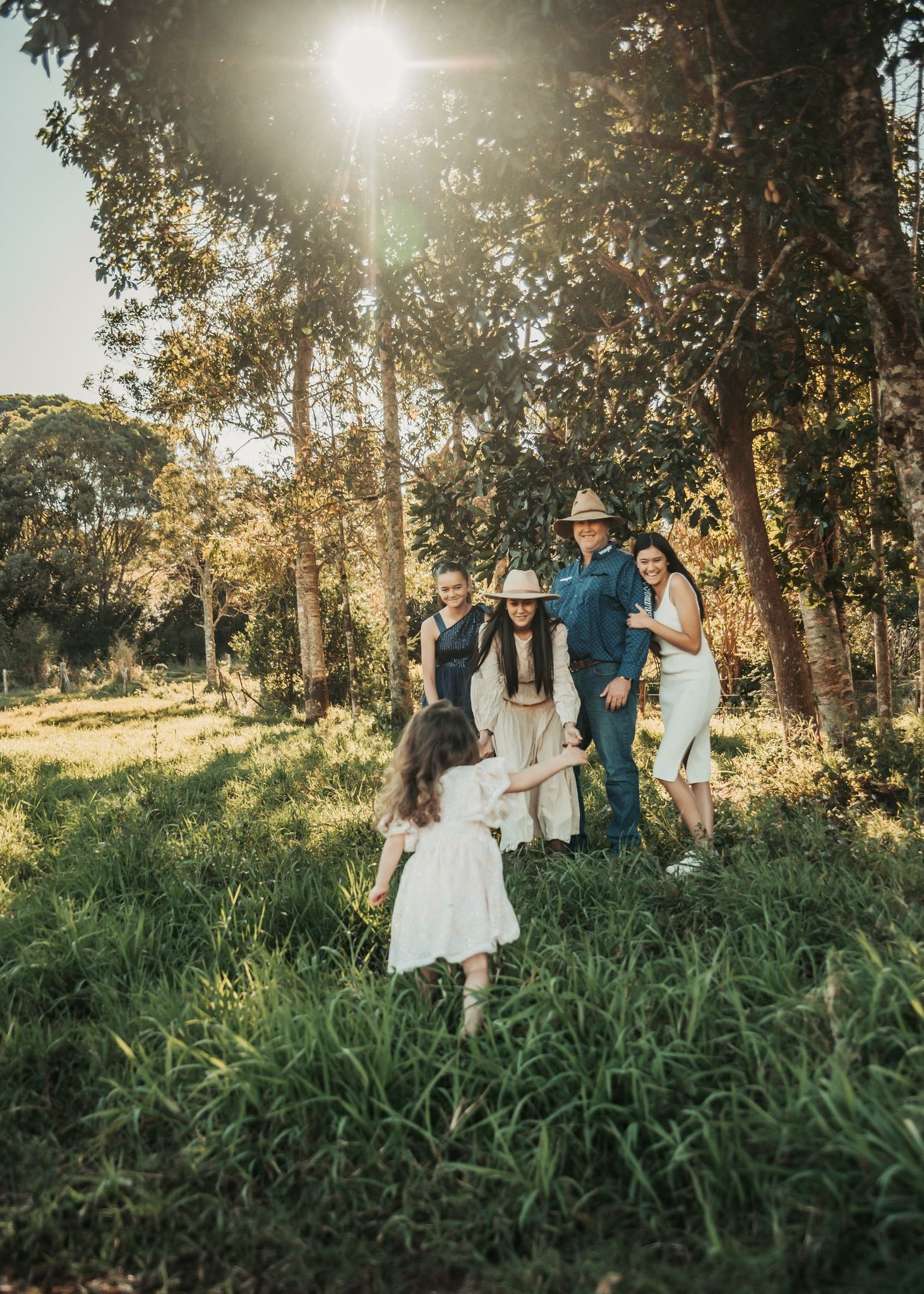Family in a Sunlit Grassy Field, Child Running Toward Them — Feathers & Lace Photography in Tarzali, QLD