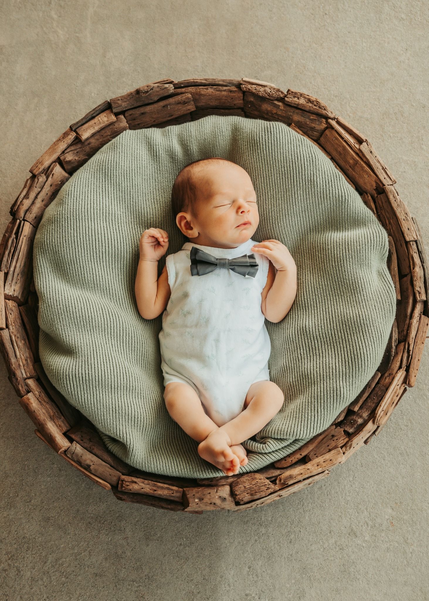 Newborn Baby in White Onesie and Bow Tie, Lying in a Wooden Basket — Feathers & Lace Photography in Tarzali, QLD