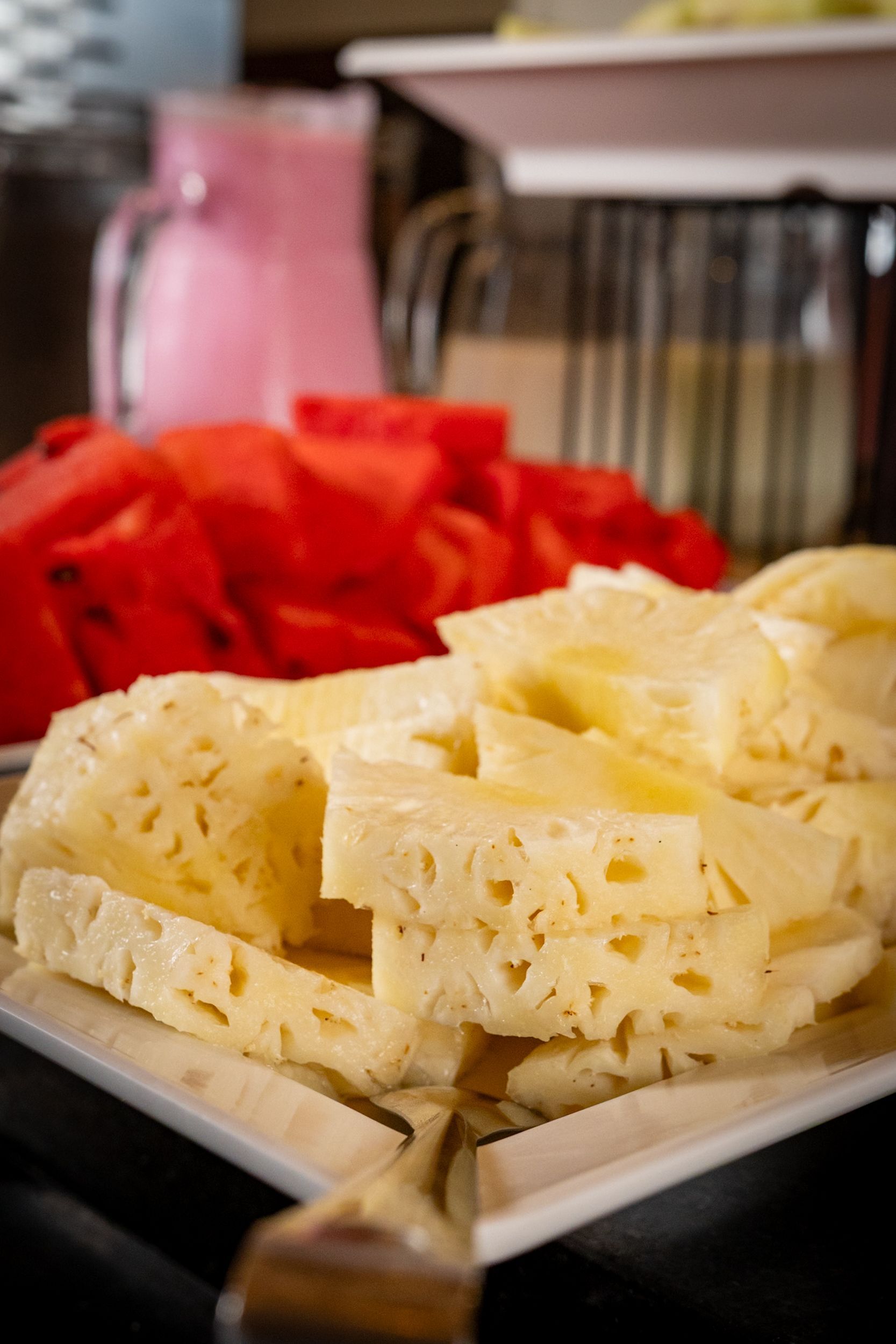 Fatias de abacaxi e melancia em um prato branco, com uma bebida rosa ao fundo.