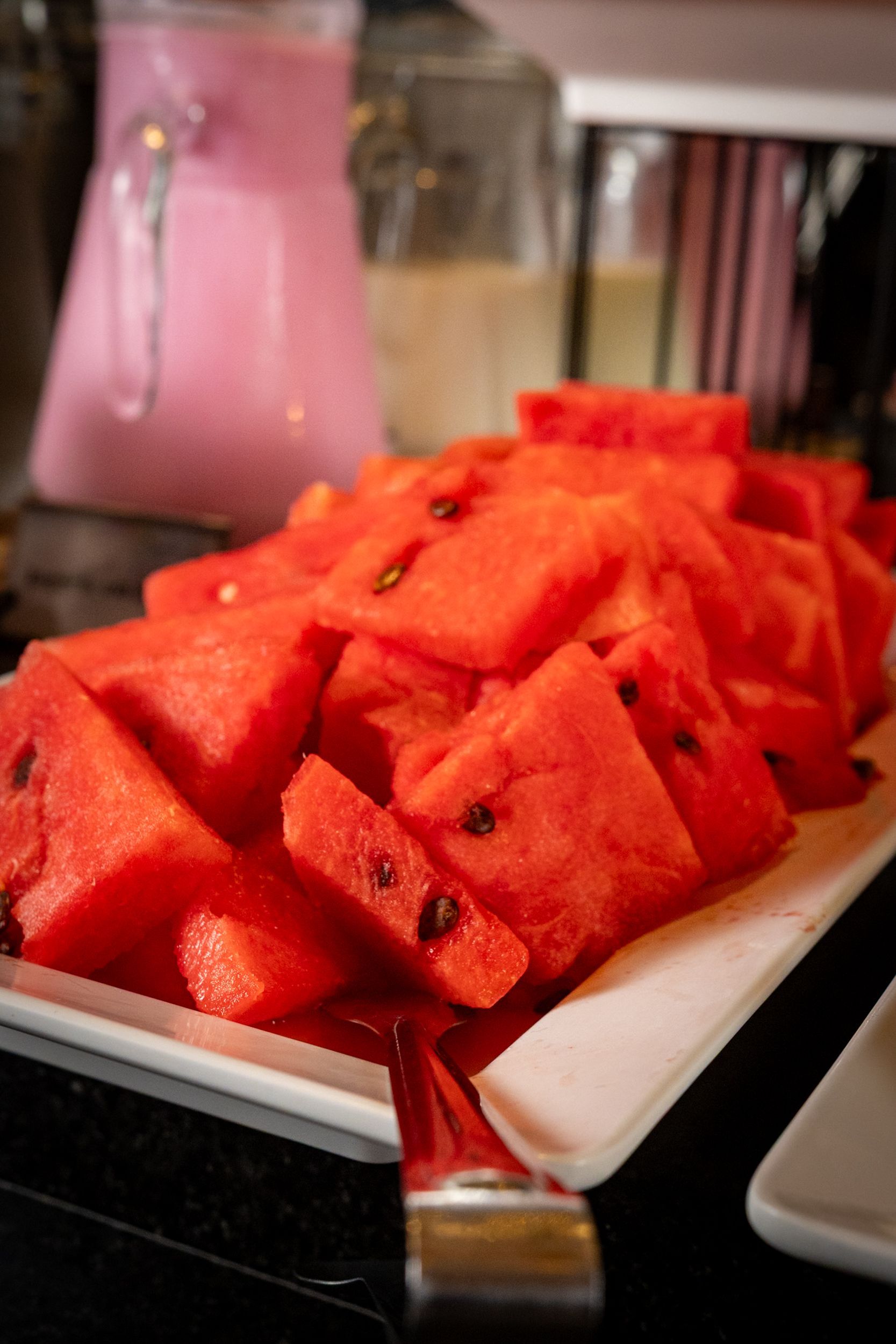 Prato com fatias de melancia e uma bebida rosa ao fundo.