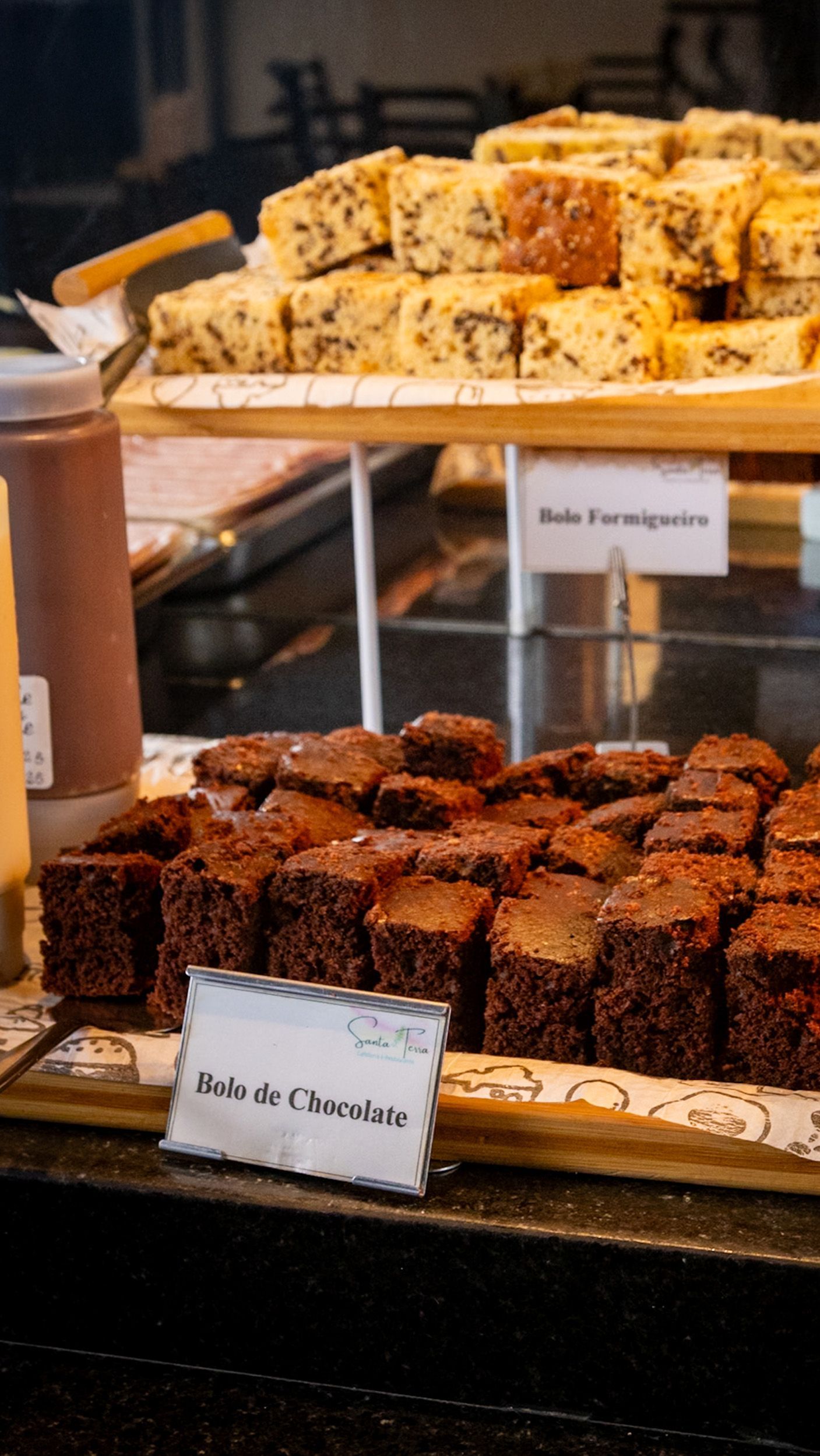 Exposição de brownies e bolos em vitrine. Placas com os dizeres 