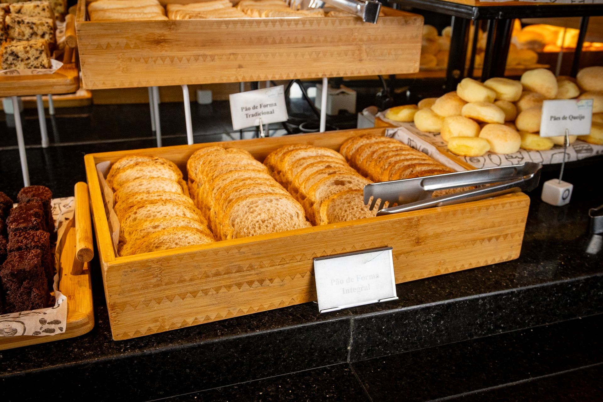 Balcão de madeira com diversas opções de pão, incluindo torradas fatiadas, pãezinhos e pão escuro.