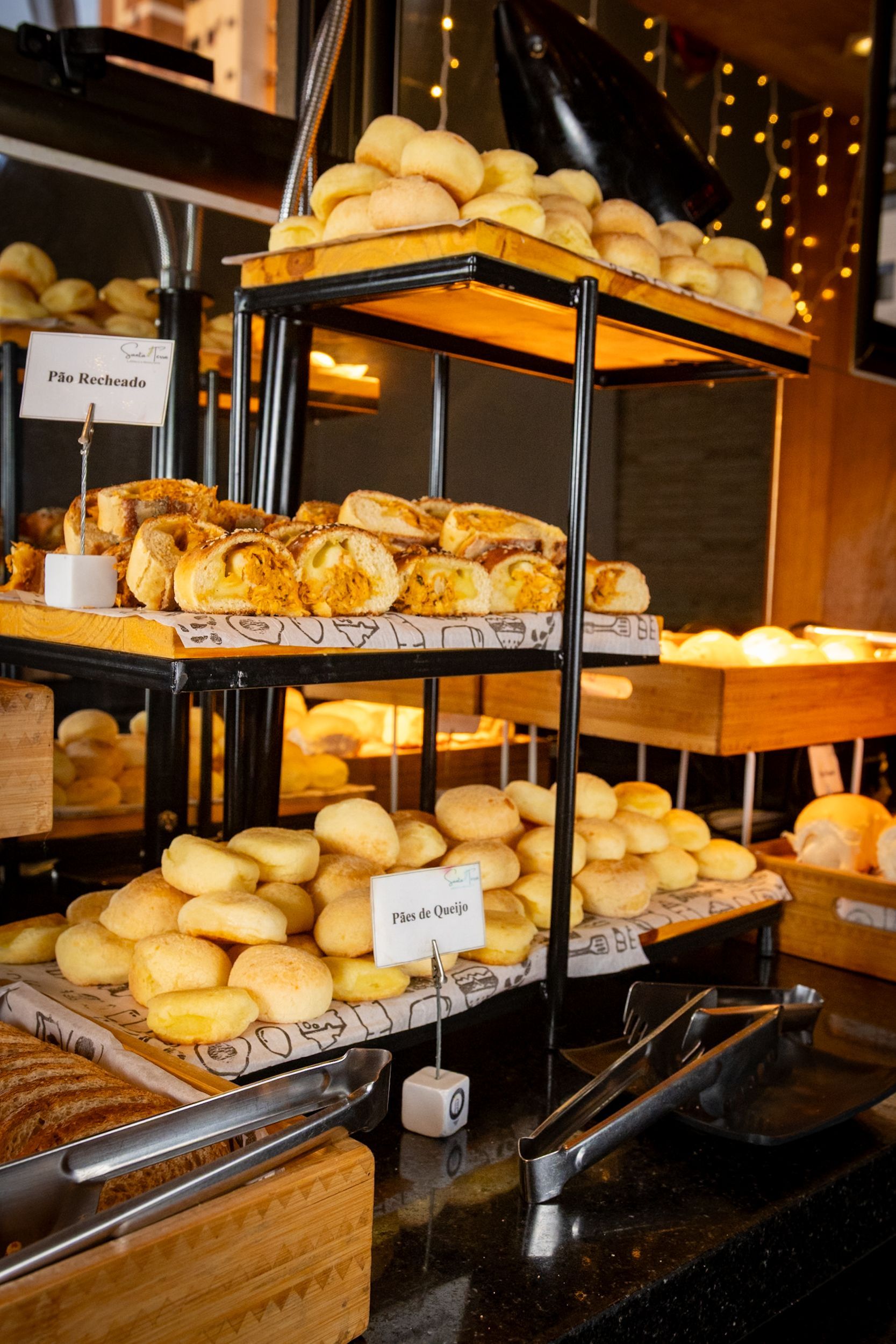 Buffet de pães com pãezinhos e doces em um suporte de metal preto de três andares.