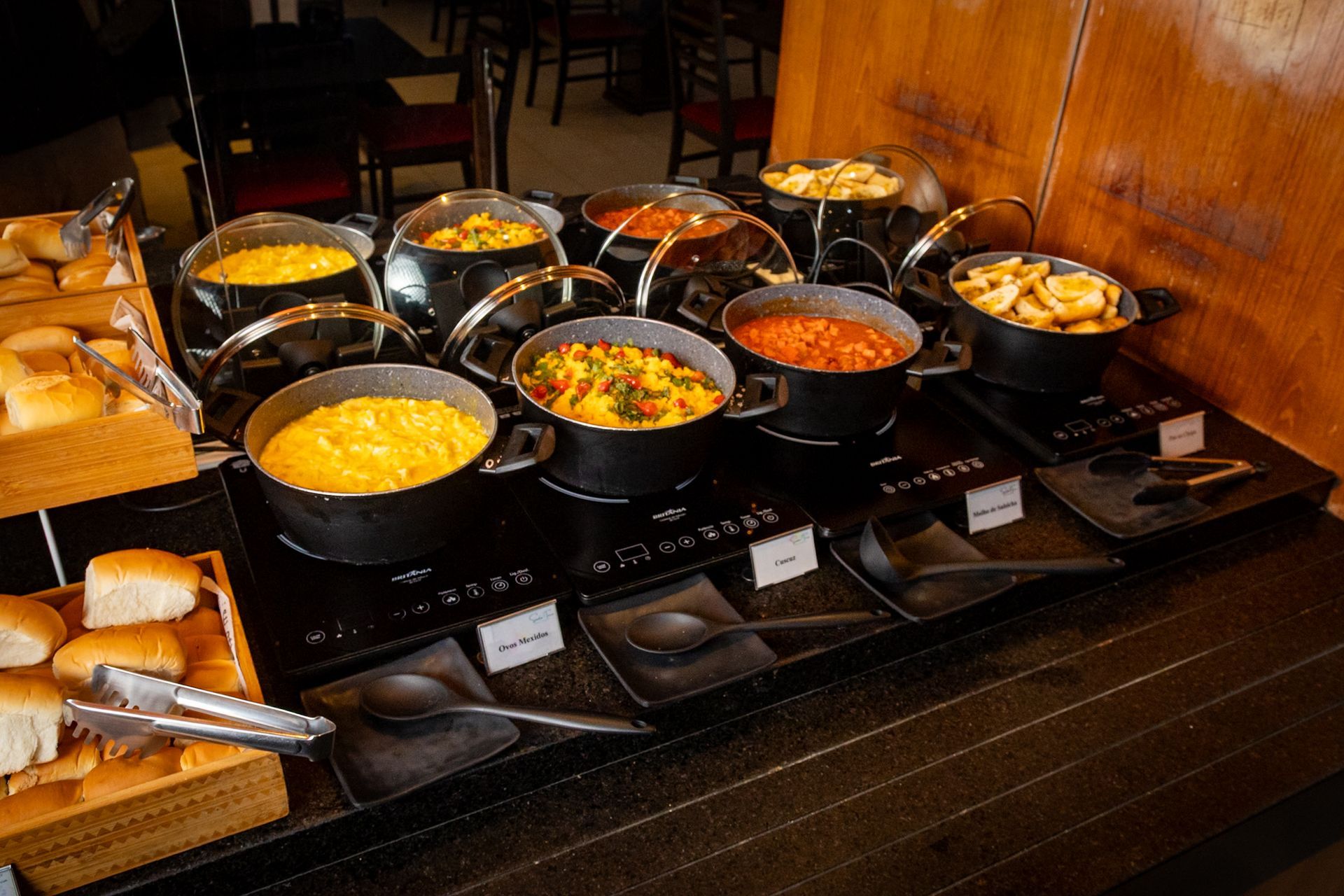 Exposição de comidas em estilo bufê: Diversos tipos de caçarolas e pães em aquecedores.