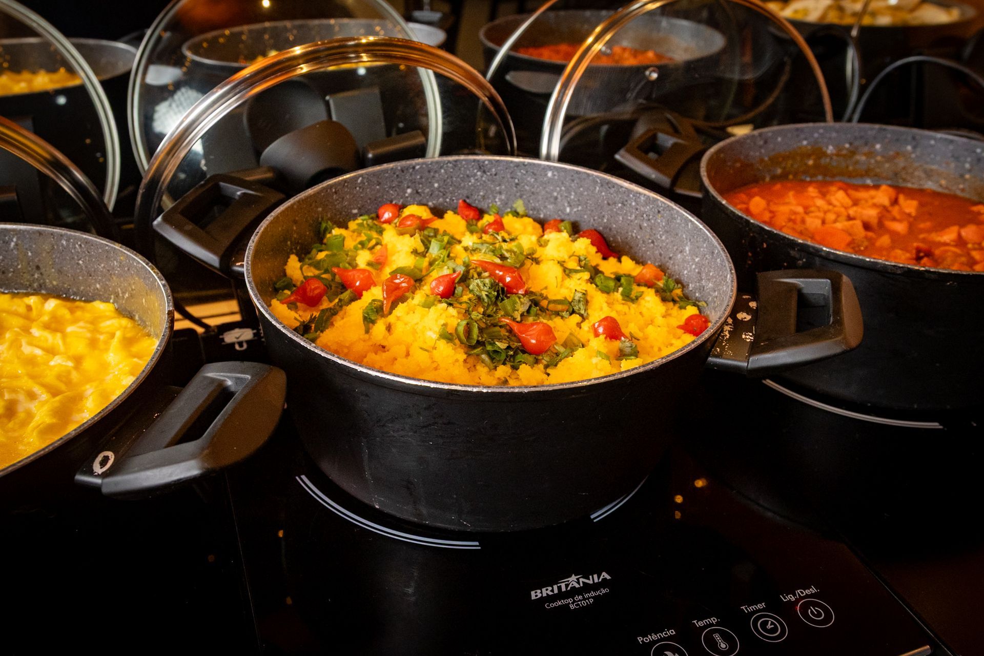 Diversos pratos, incluindo cuscuz, em panelas pretas em um bufê.