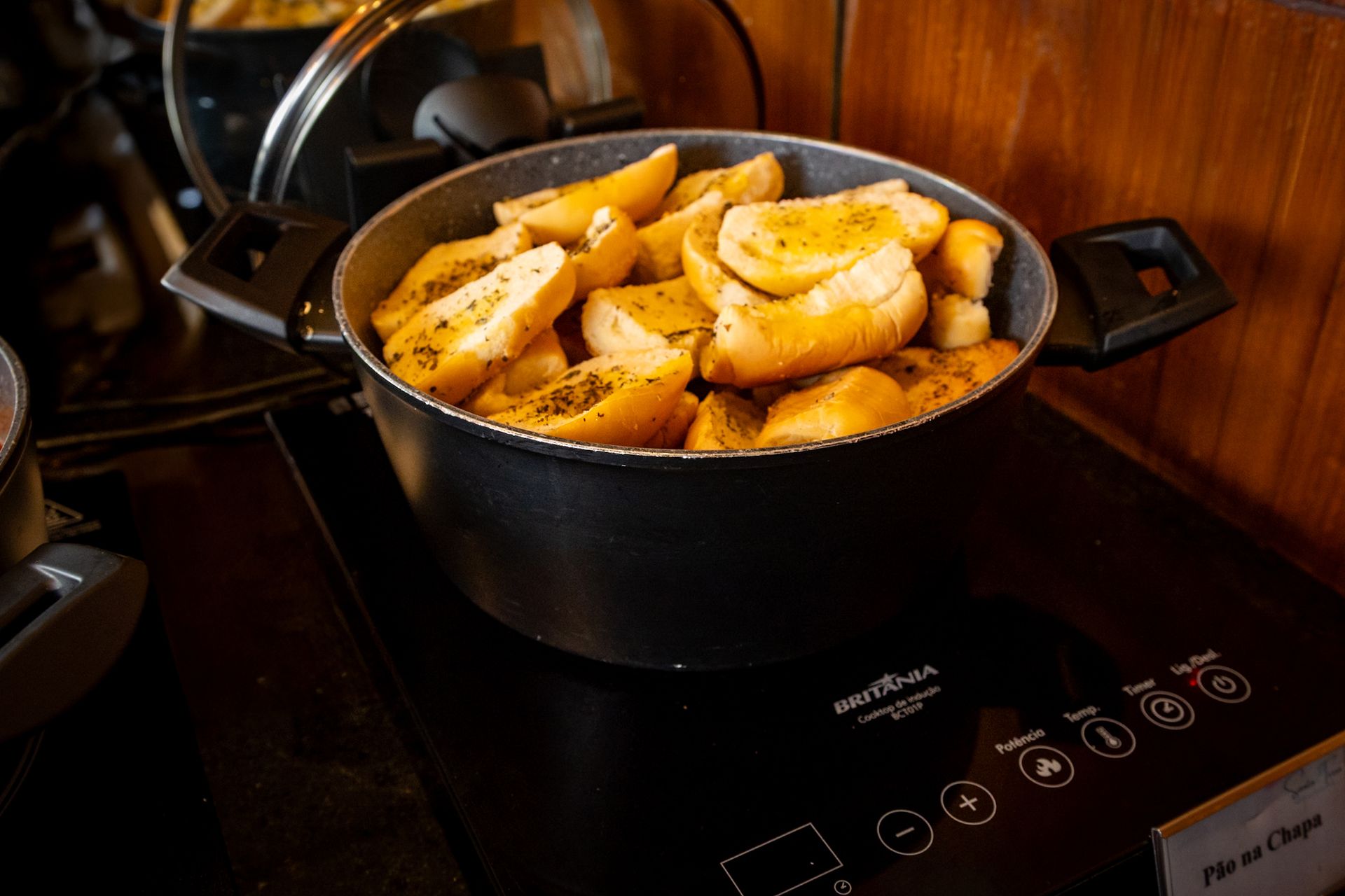 Panela de pão de alho dourado sobre uma bancada preta; um eletrodoméstico está embaixo.
